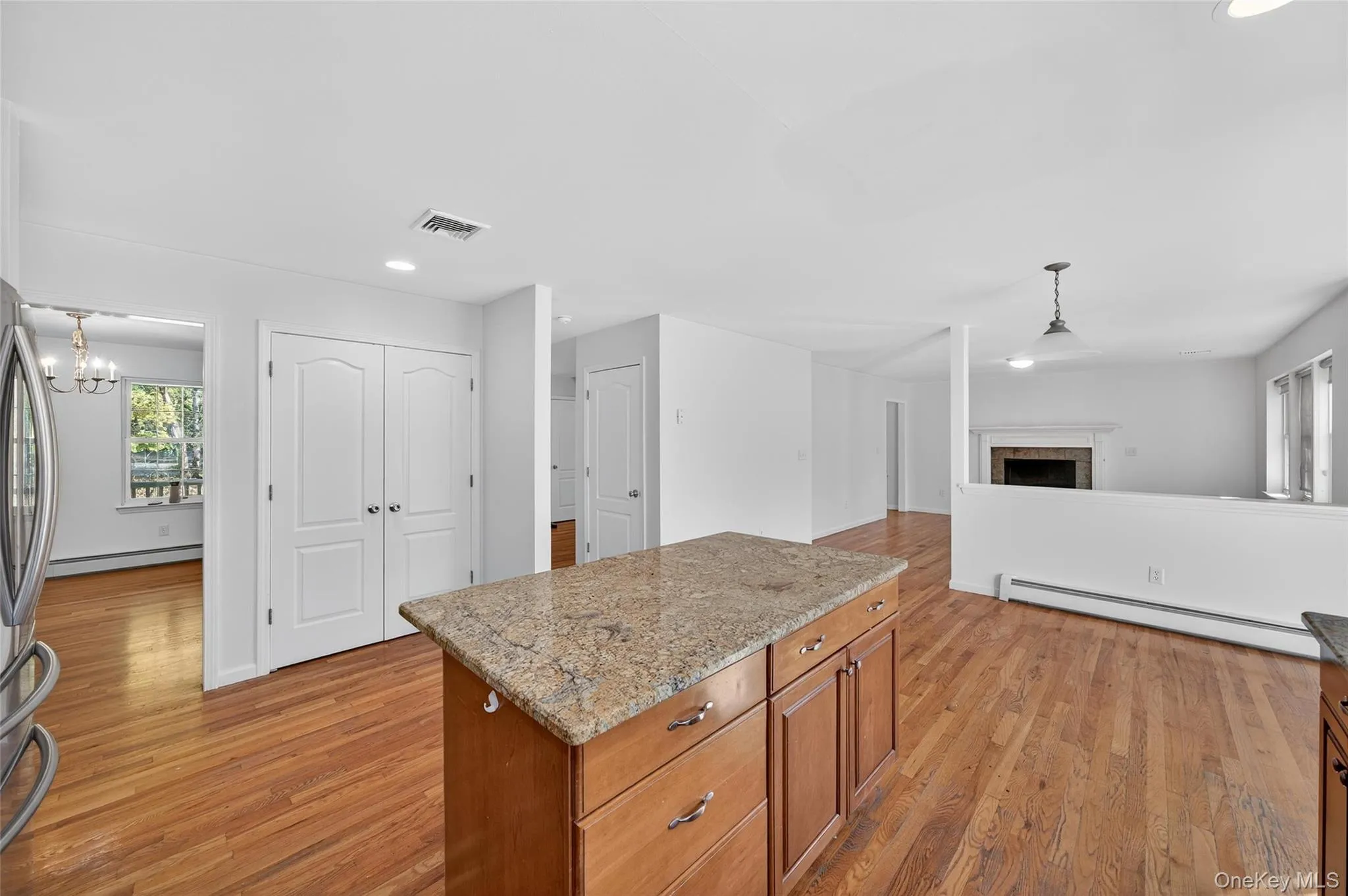 Kitchen with hanging light fixtures, brown cabinets, a kitchen island, light stone counters, and light wood-style floors Kitchen with hanging light fixtures, brown cabinets, a kitchen island, light stone counters, and light wood-style floors