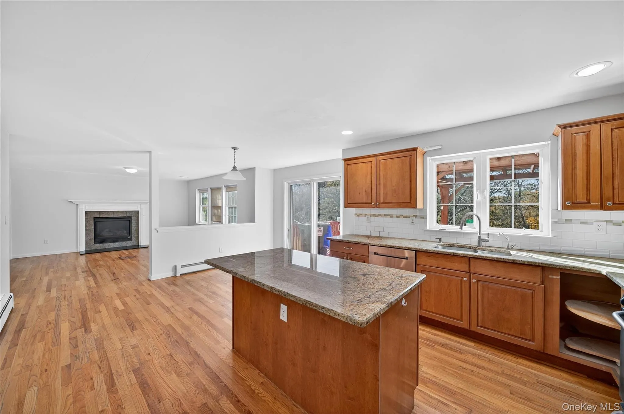 Kitchen featuring brown cabinetry, a kitchen island, tasteful backsplash, light stone counters, and plenty of natural light Kitchen featuring brown cabinetry, a kitchen island, tasteful backsplash, light stone counters, and plenty of natural light