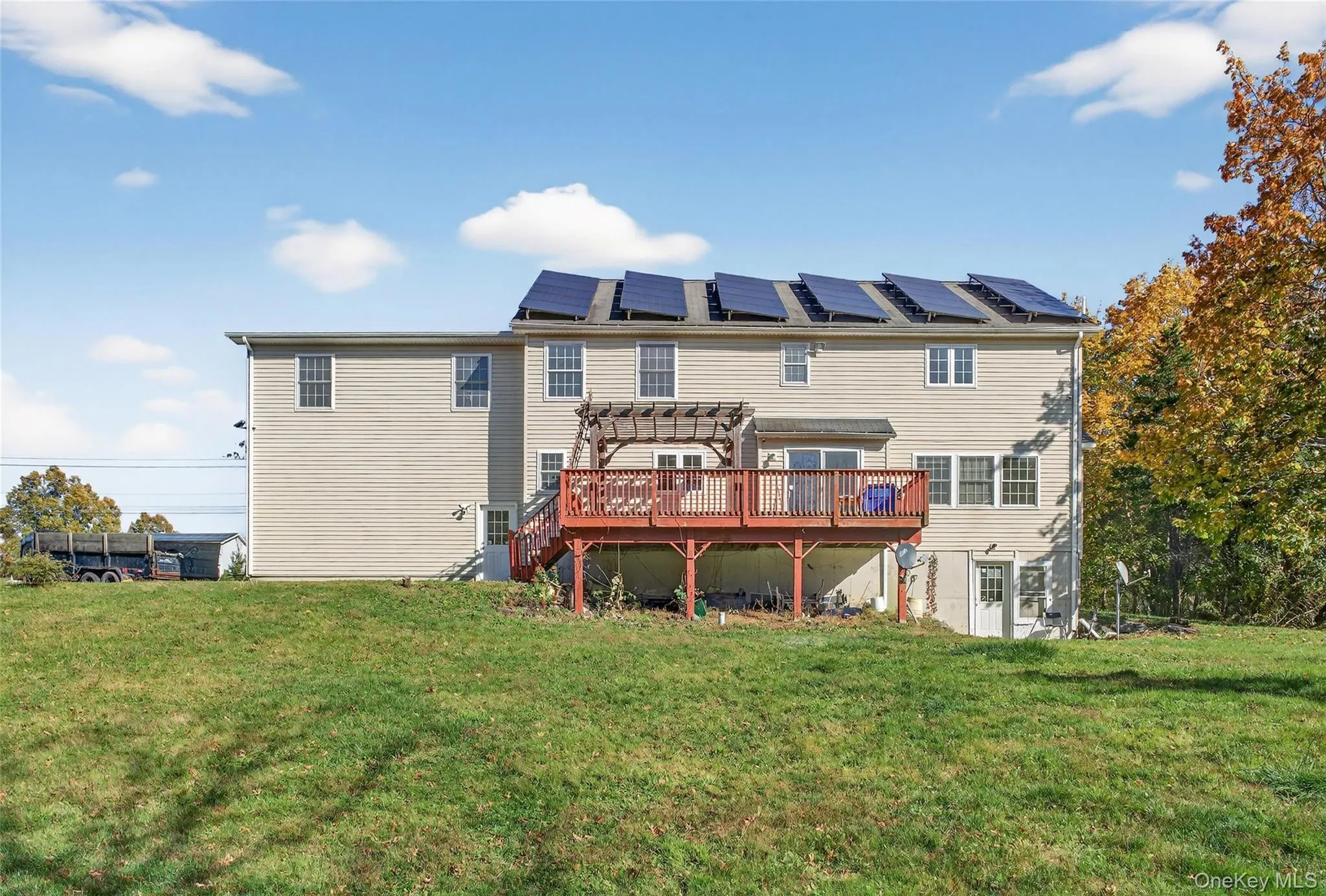 Back of property with a wooden deck, a lawn, and a pergola Back of property with a wooden deck, a lawn, and a pergola