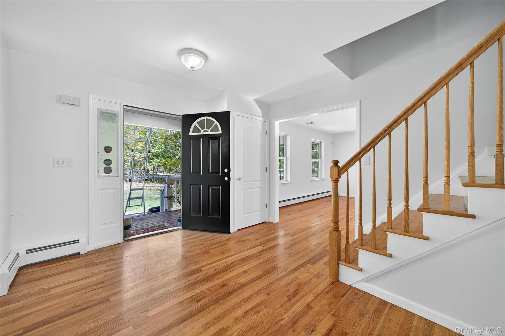 Foyer entrance with light wood-style flooring, stairway, and baseboard heating Foyer entrance with light wood-style flooring, stairway, and baseboard heating