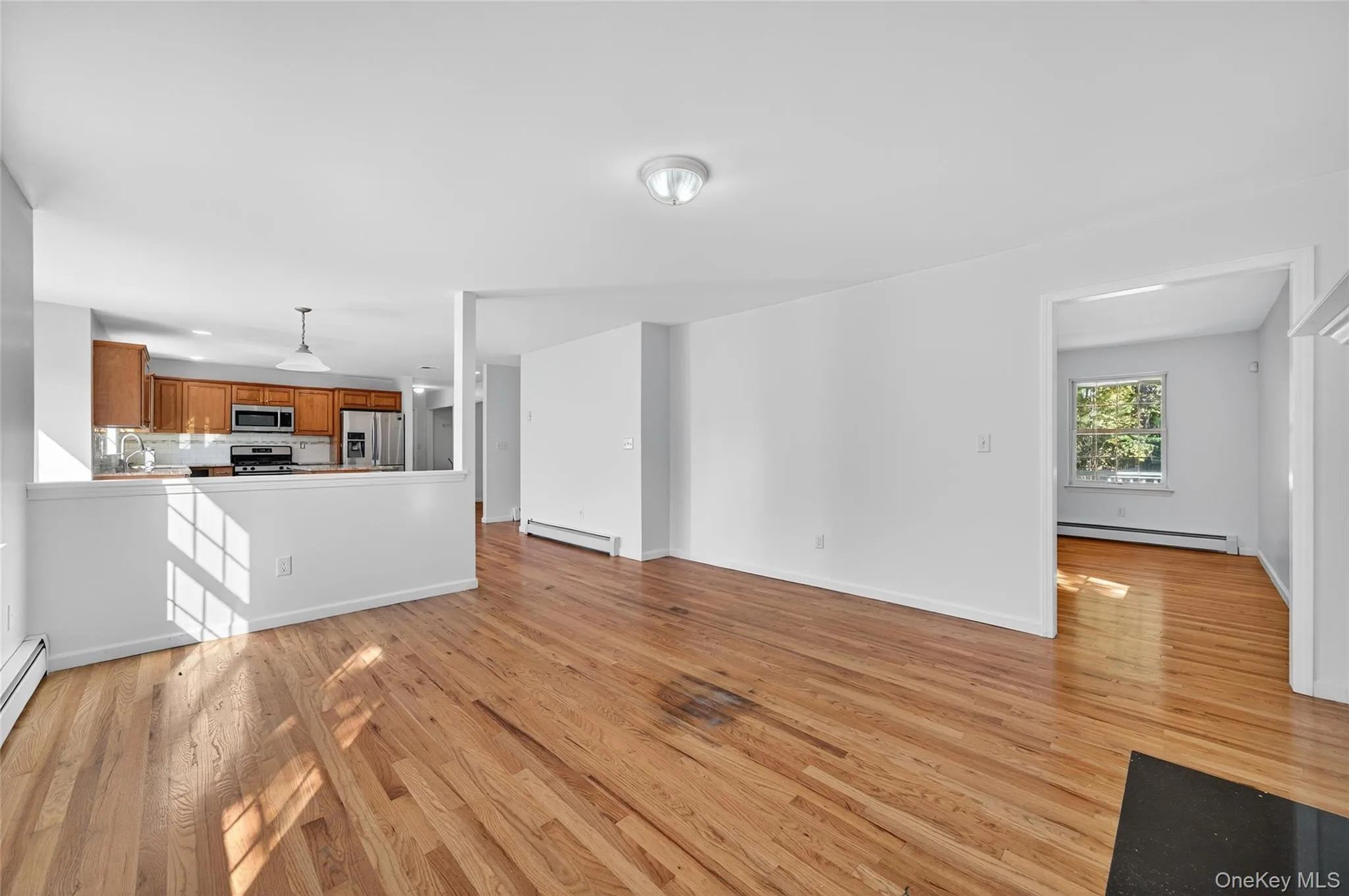 Unfurnished living room with light wood-style flooring and a baseboard heating unit Unfurnished living room with light wood-style flooring and a baseboard heating unit