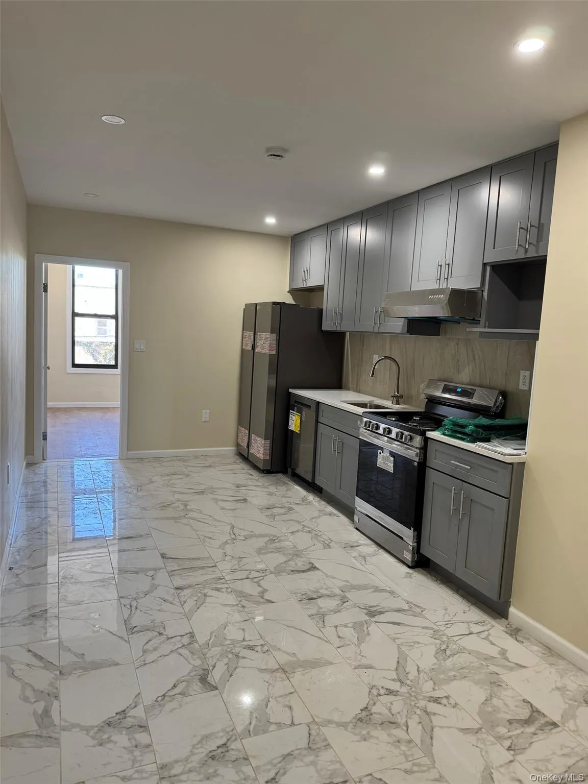 Kitchen featuring light marble finish flooring, appliances with stainless steel finishes, light countertops, gray cabinetry, and backsplash Kitchen featuring light marble finish flooring, appliances with stainless steel finishes, light countertops, gray cabinetry, and backsplash