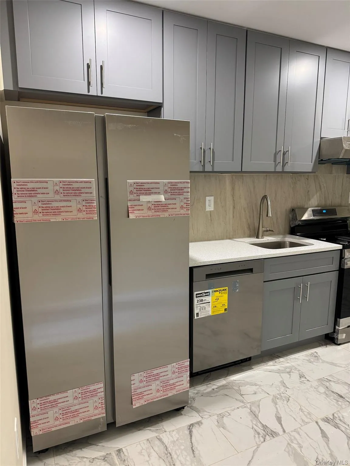 Kitchen featuring gray cabinets, appliances with stainless steel finishes, light marble finish floors, extractor fan, and light stone counters Kitchen featuring gray cabinets, appliances with stainless steel finishes, light marble finish floors, extractor fan, and light stone counters