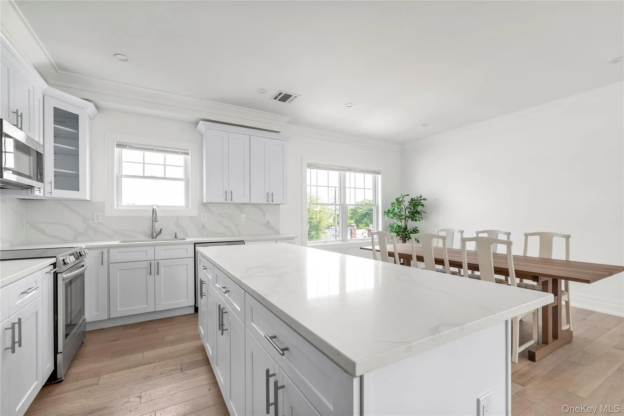Kitchen with stainless steel appliances, plenty of natural light, light wood-type flooring, ornamental molding, and backsplash Kitchen with stainless steel appliances, plenty of natural light, light wood-type flooring, ornamental molding, and backsplash