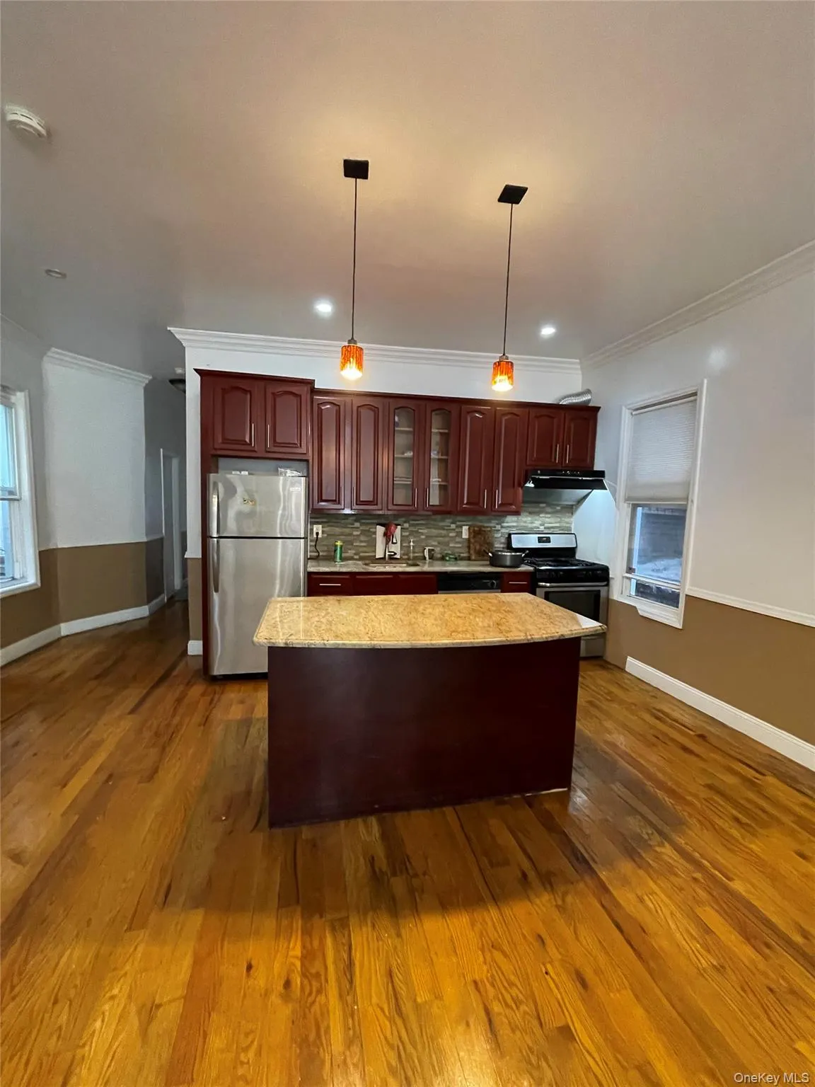 Kitchen with ornamental molding, hanging light fixtures, appliances with stainless steel finishes, a center island, and tasteful backsplash Kitchen with ornamental molding, hanging light fixtures, appliances with stainless steel finishes, a center island, and tasteful backsplash