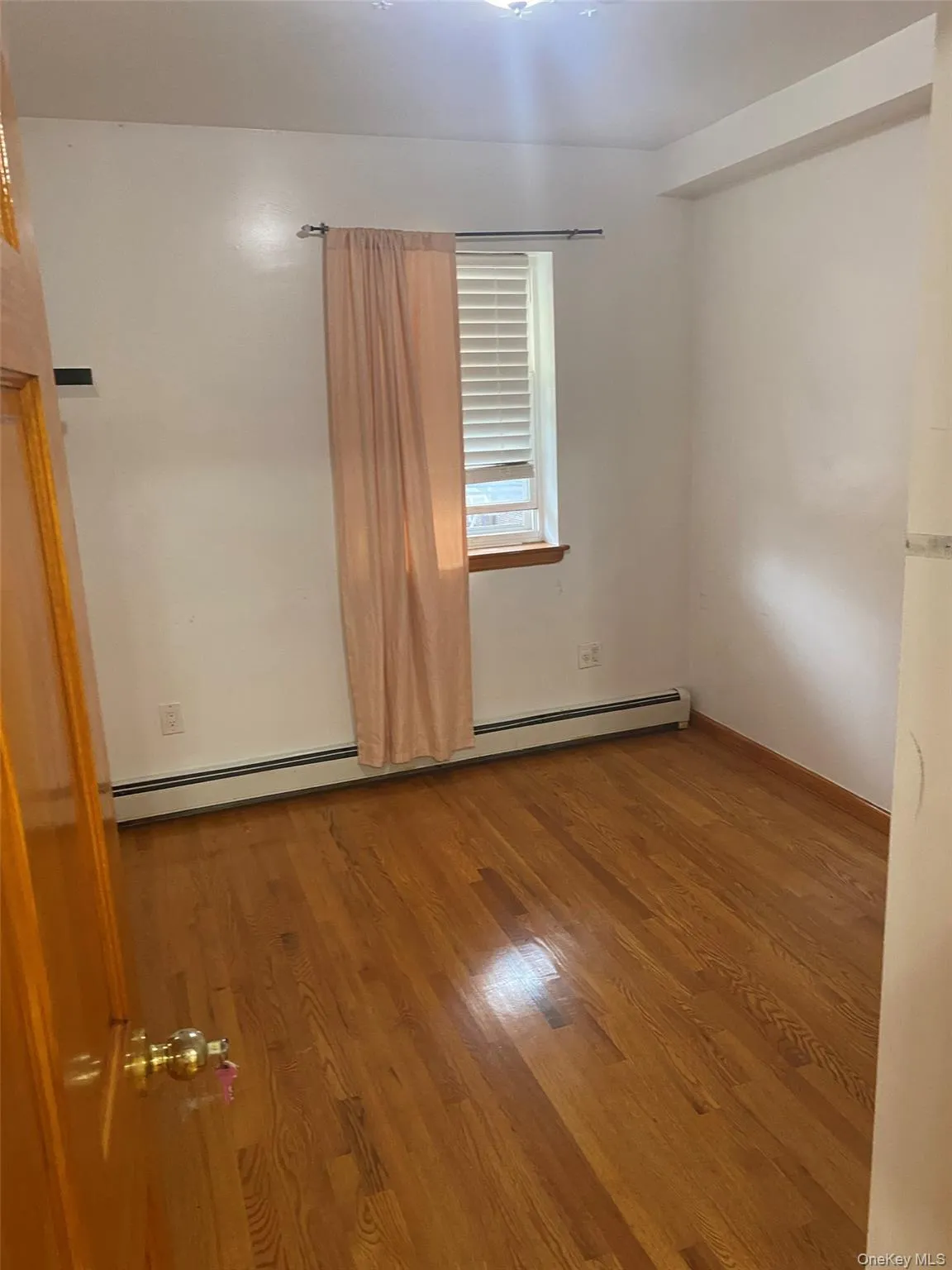 Empty room with wood finished floors and a baseboard heating unit Empty room with wood finished floors and a baseboard heating unit