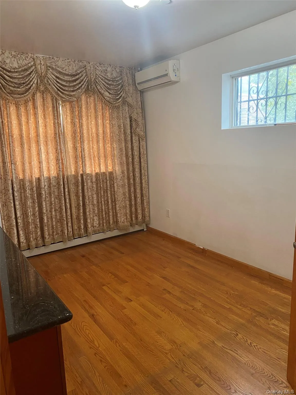 Empty room with wood finished floors, a wall mounted air conditioner, and baseboard heating Empty room with wood finished floors, a wall mounted air conditioner, and baseboard heating