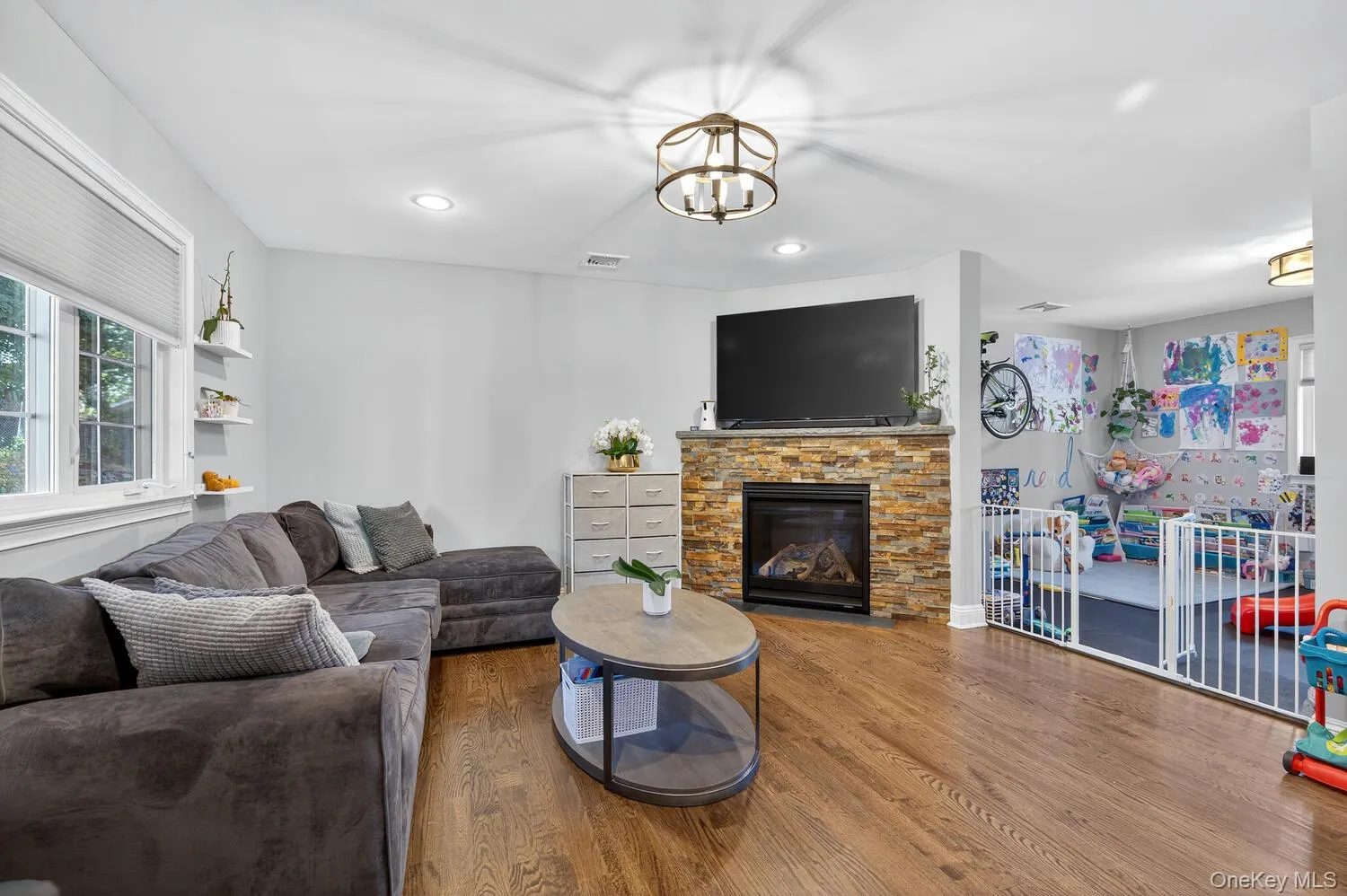 Living room featuring wood finished floors, a stone fireplace, recessed lighting, and a chandelier Living room featuring wood finished floors, a stone fireplace, recessed lighting, and a chandelier