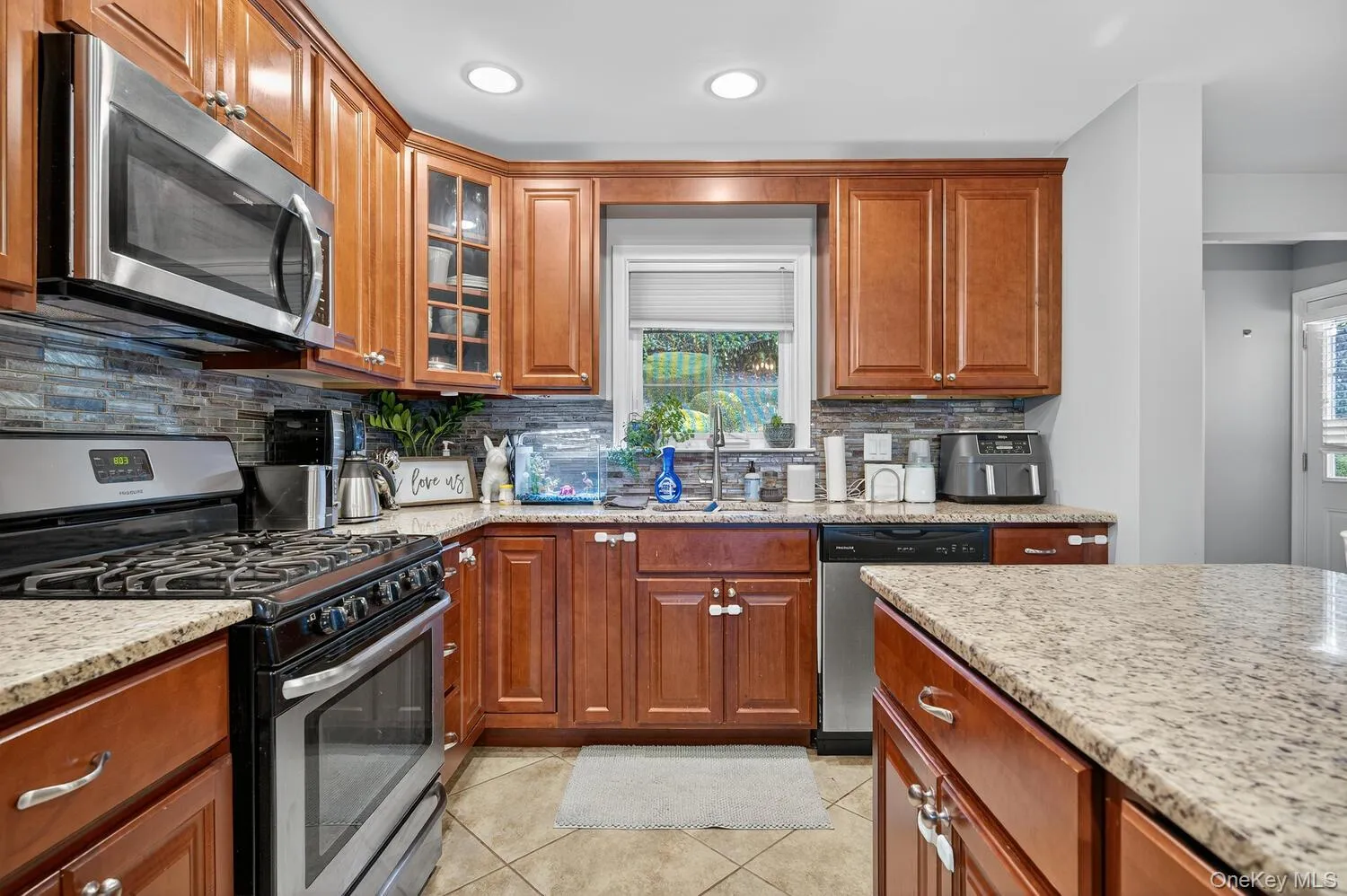 Kitchen with stainless steel appliances, brown cabinets, decorative backsplash, light tile patterned floors, and recessed lighting Kitchen with stainless steel appliances, brown cabinets, decorative backsplash, light tile patterned floors, and recessed lighting