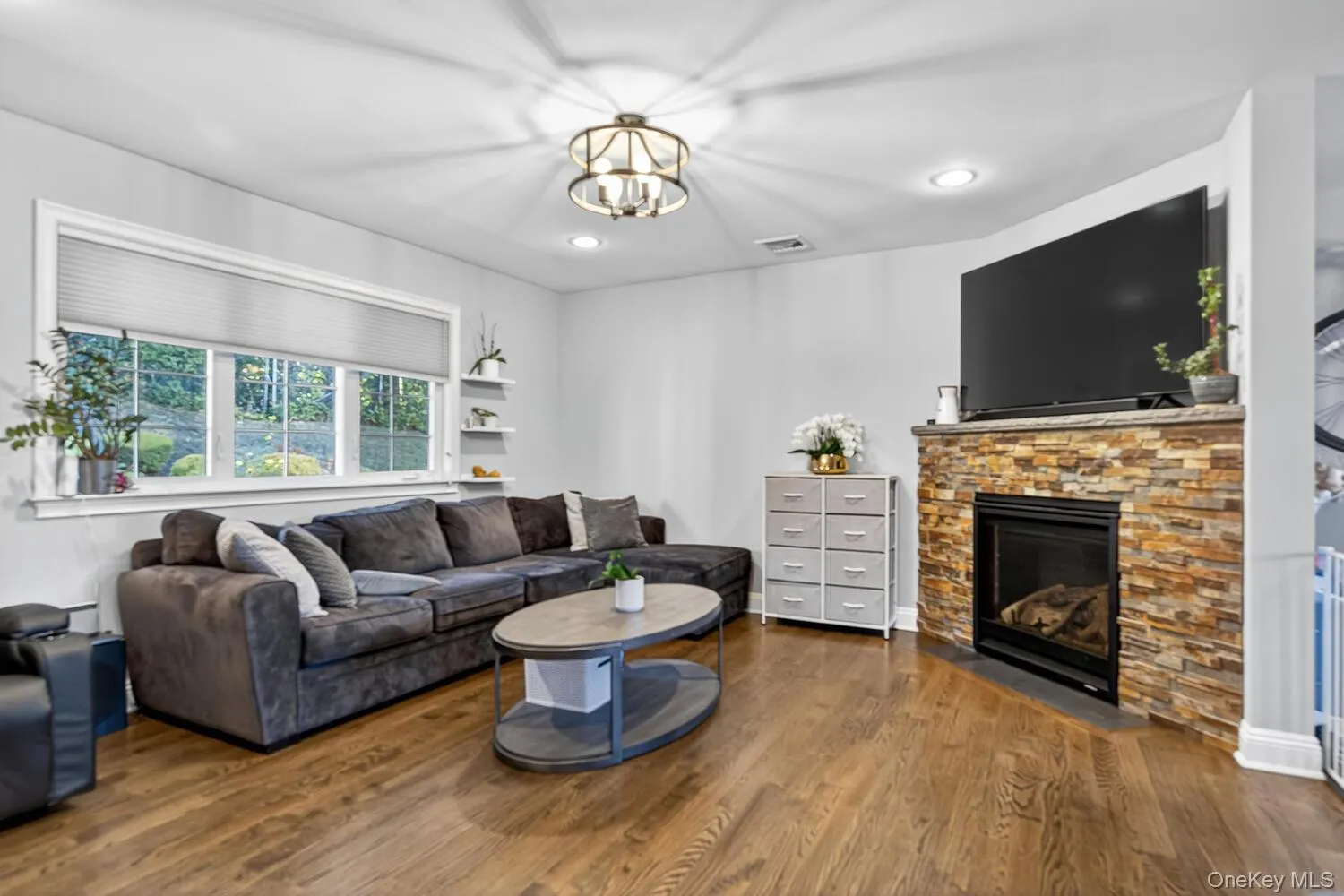 Living room with dark wood-style flooring, a stone fireplace, recessed lighting, and a chandelier Living room with dark wood-style flooring, a stone fireplace, recessed lighting, and a chandelier