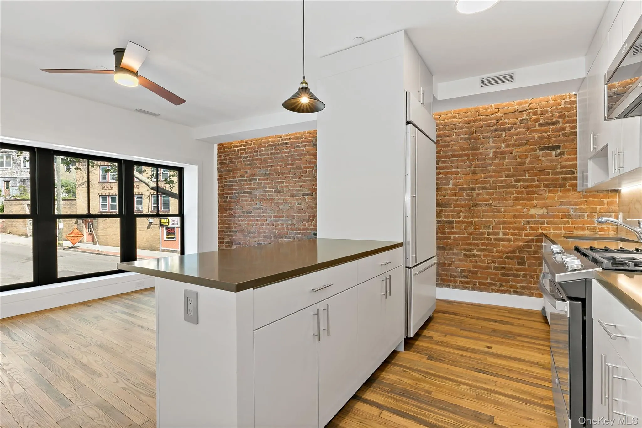 Kitchen featuring brick wall, white cabinets, pendant lighting, stainless steel gas range, and light wood-style floors Kitchen featuring brick wall, white cabinets, pendant lighting, stainless steel gas range, and light wood-style floors