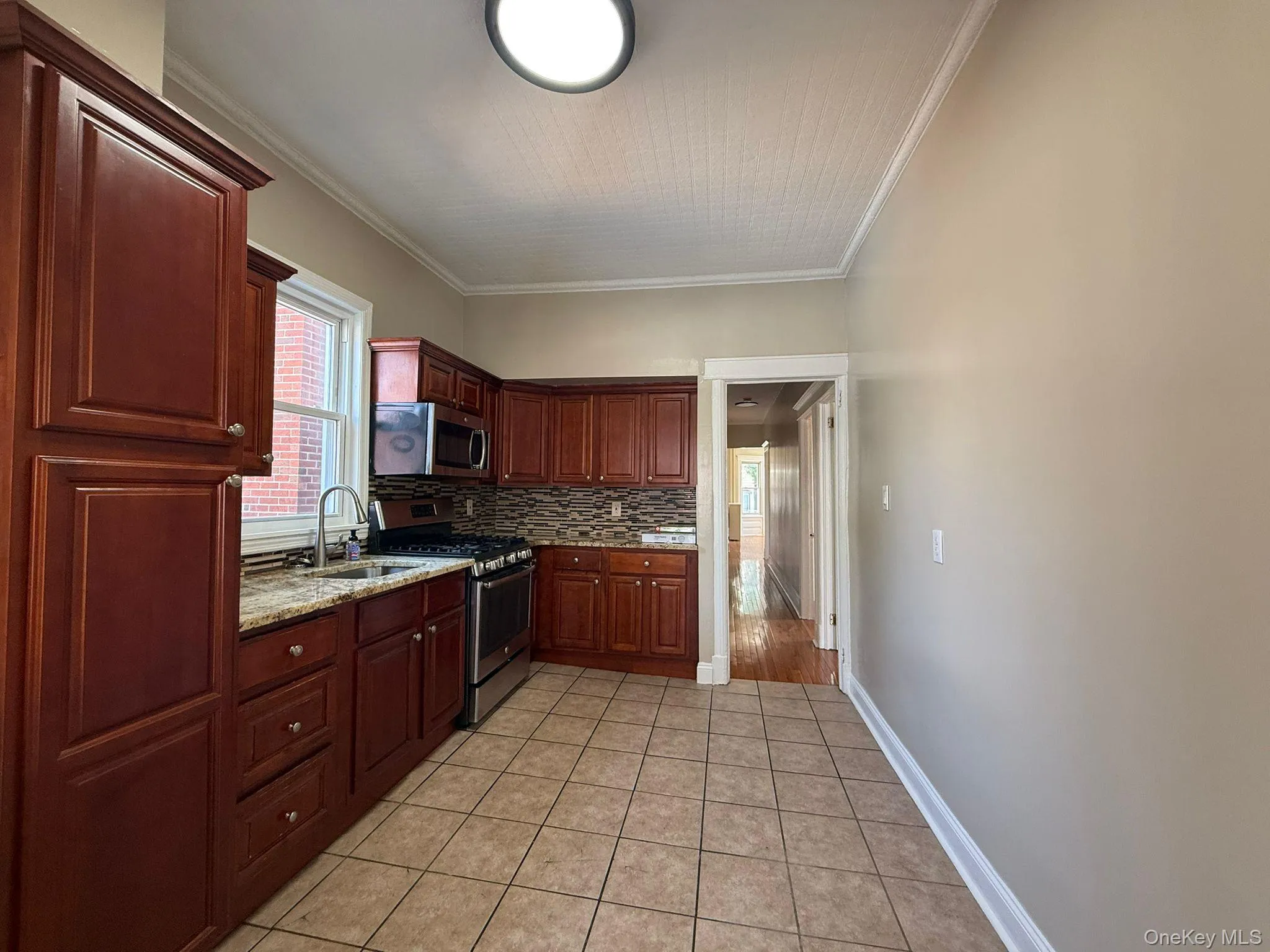 Kitchen featuring appliances with stainless steel finishes, crown molding, decorative backsplash, light stone countertops, and light tile patterned floors Kitchen featuring appliances with stainless steel finishes, crown molding, decorative backsplash, light stone countertops, and light tile patterned floors