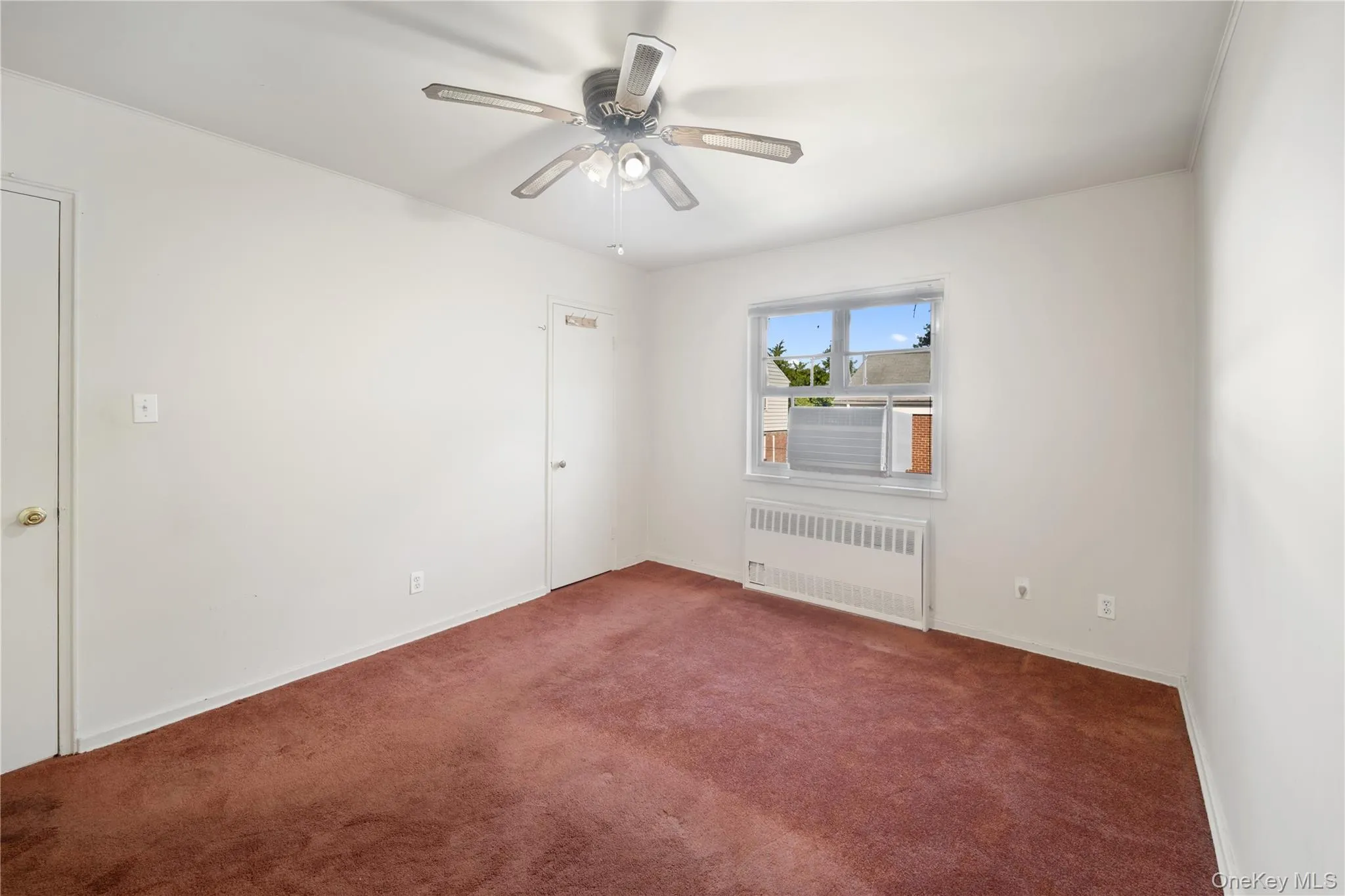Unfurnished room with radiator, carpet flooring, and a ceiling fan Unfurnished room with radiator, carpet flooring, and a ceiling fan