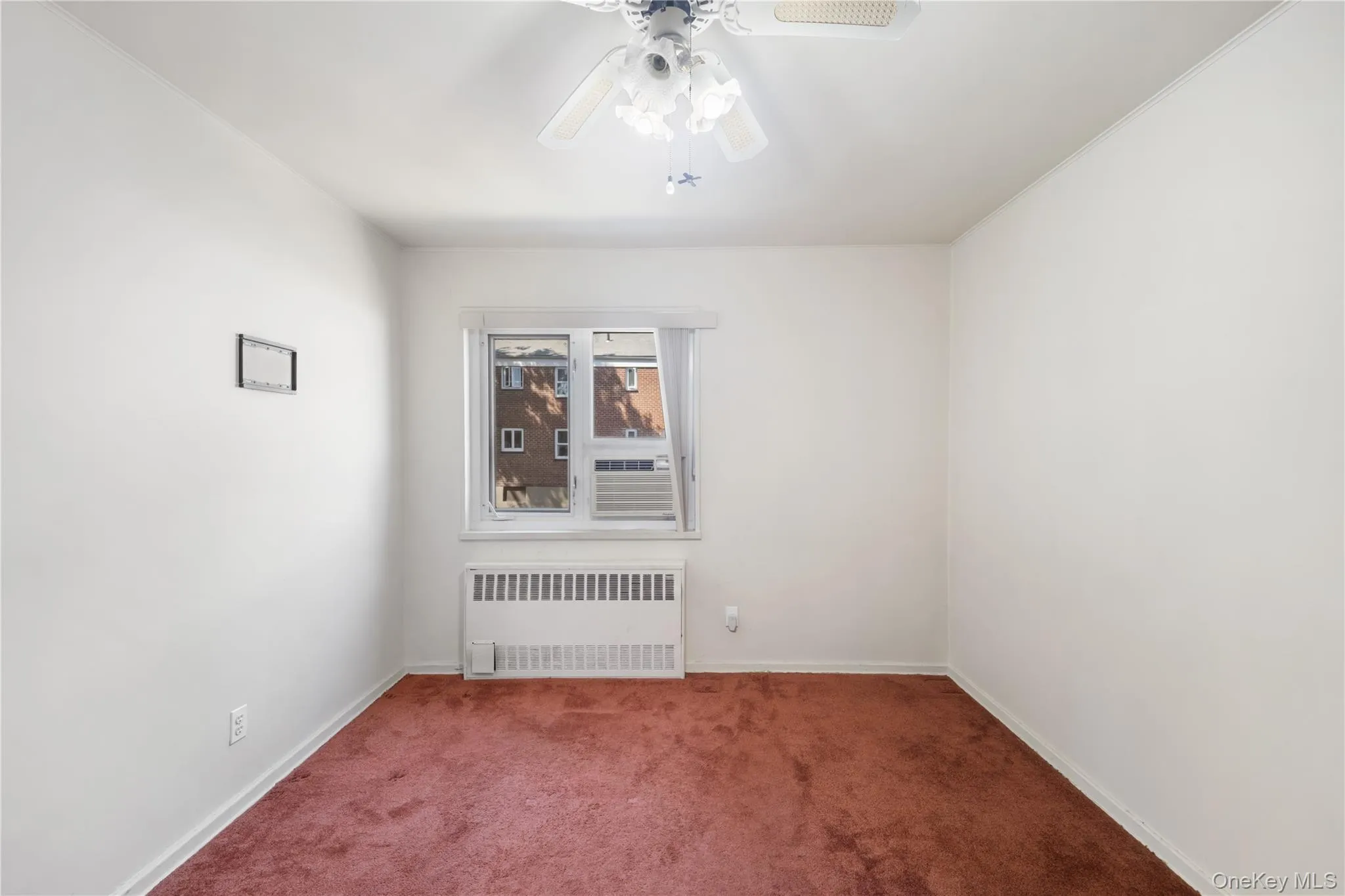 Empty room with radiator heating unit, carpet flooring, and a ceiling fan Empty room with radiator heating unit, carpet flooring, and a ceiling fan