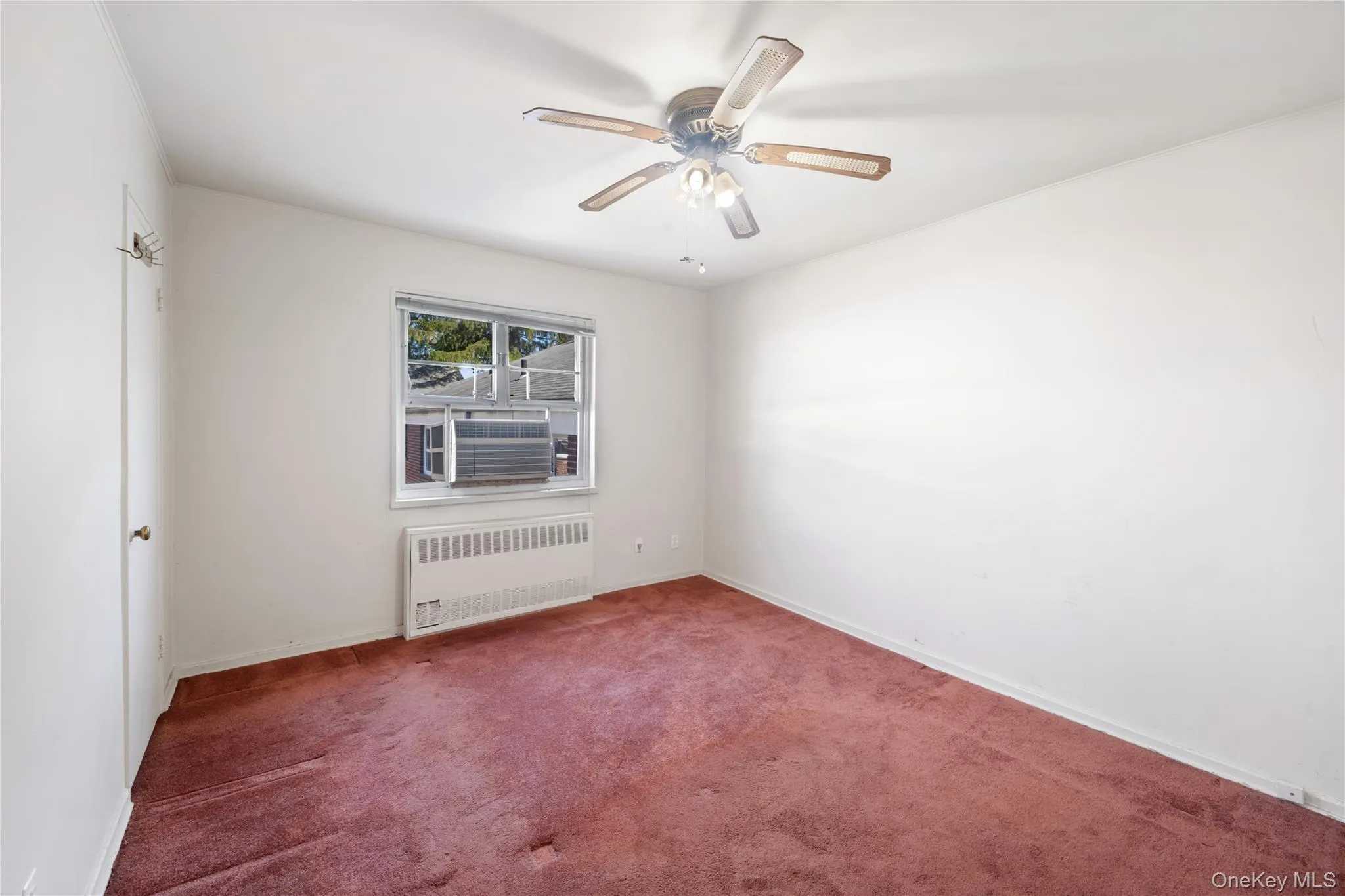 Carpeted spare room featuring radiator and ceiling fan Carpeted spare room featuring radiator and ceiling fan