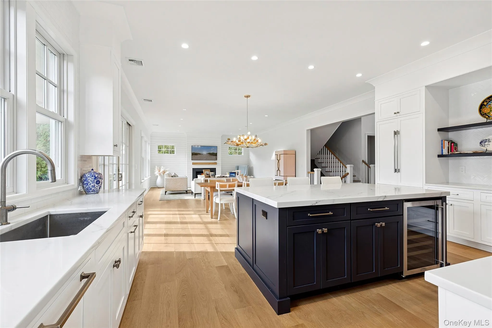 Kitchen featuring white cabinetry, light stone counters, backsplash, light wood-style flooring, and wine cooler Kitchen featuring white cabinetry, light stone counters, backsplash, light wood-style flooring, and wine cooler