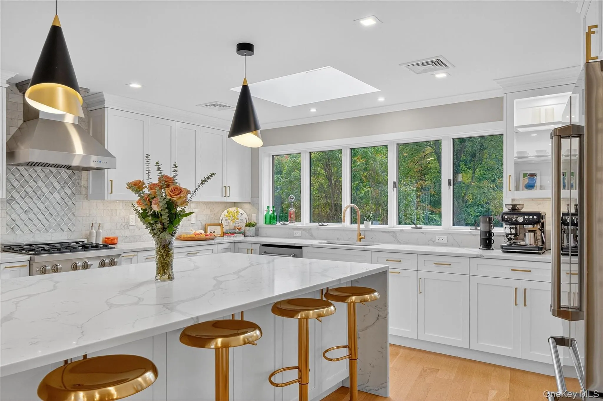 Kitchen featuring a skylight, white cabinets, light stone countertops, decorative light fixtures, and a kitchen bar Kitchen featuring a skylight, white cabinets, light stone countertops, decorative light fixtures, and a kitchen bar