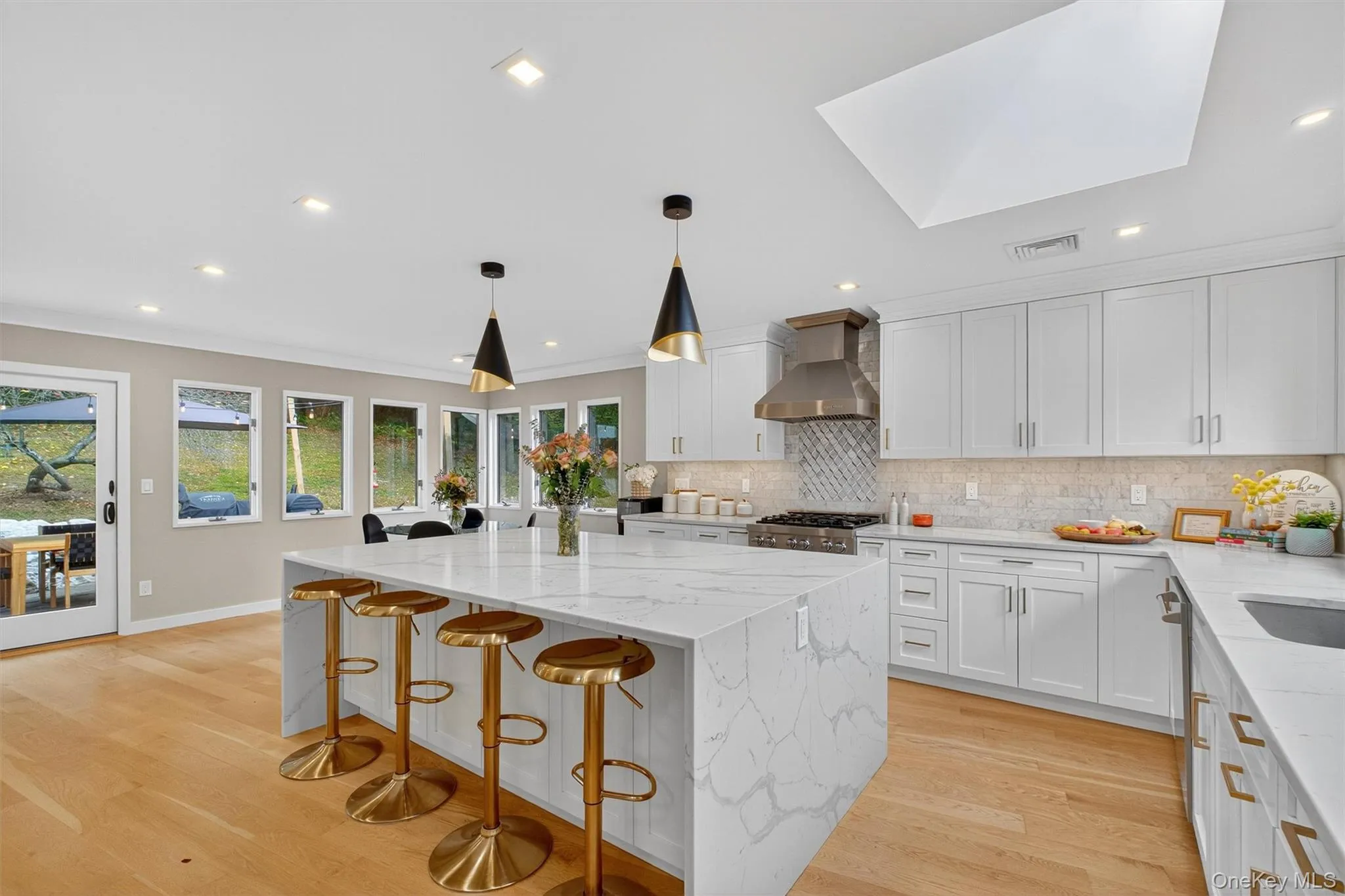 Kitchen with light stone counters, tasteful backsplash, a kitchen island, hanging light fixtures, and white cabinetry Kitchen with light stone counters, tasteful backsplash, a kitchen island, hanging light fixtures, and white cabinetry