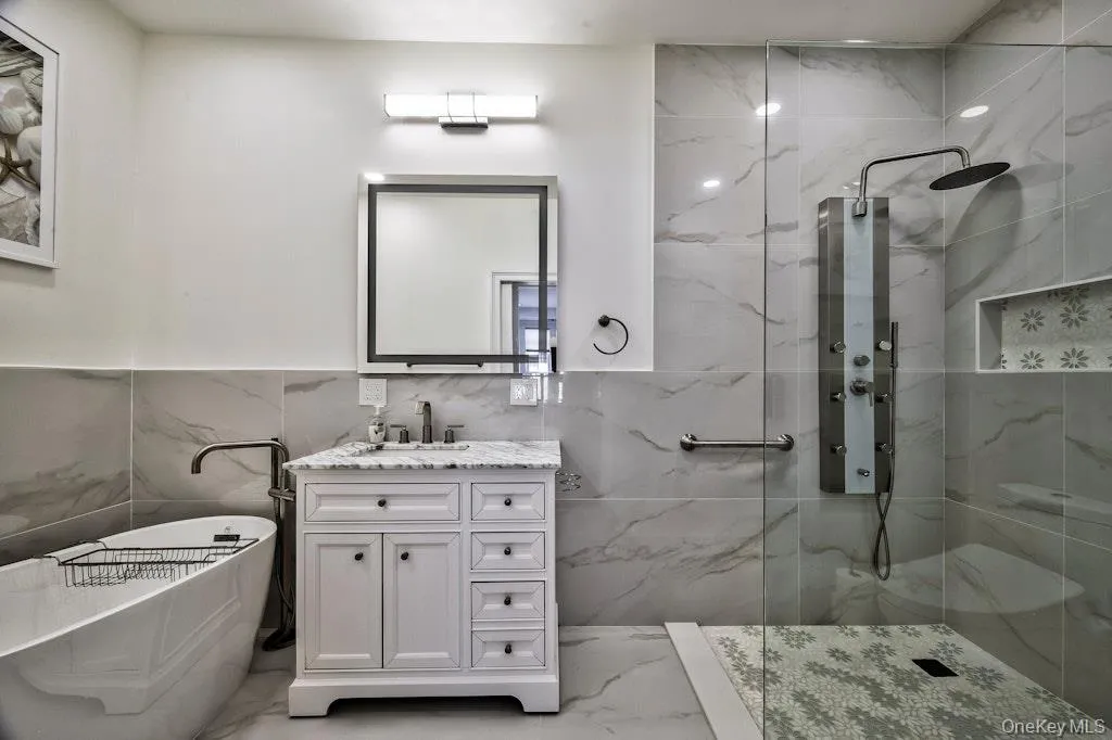 Full bathroom featuring a freestanding bath, vanity, a marble finish shower, marble tiled floors, and tile walls Full bathroom featuring a freestanding bath, vanity, a marble finish shower, marble tiled floors, and tile walls