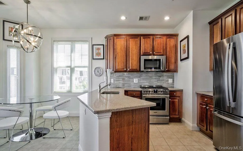 Kitchen with appliances with stainless steel finishes, a peninsula, light tile patterned floors, decorative backsplash, and light stone countertops Kitchen with appliances with stainless steel finishes, a peninsula, light tile patterned floors, decorative backsplash, and light stone countertops