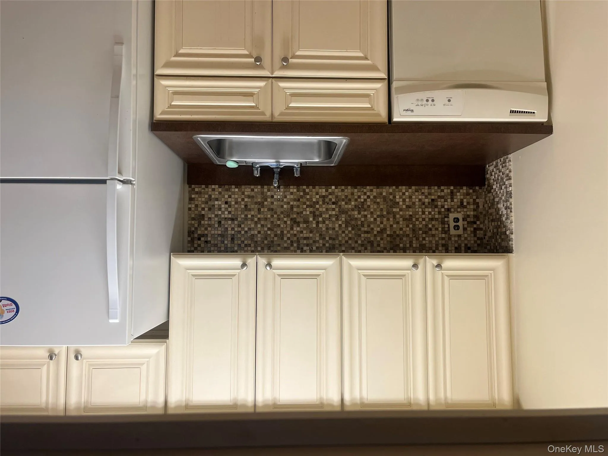 Kitchen featuring decorative backsplash, fridge, dark countertops, and dishwashing machine Kitchen featuring decorative backsplash, fridge, dark countertops, and dishwashing machine