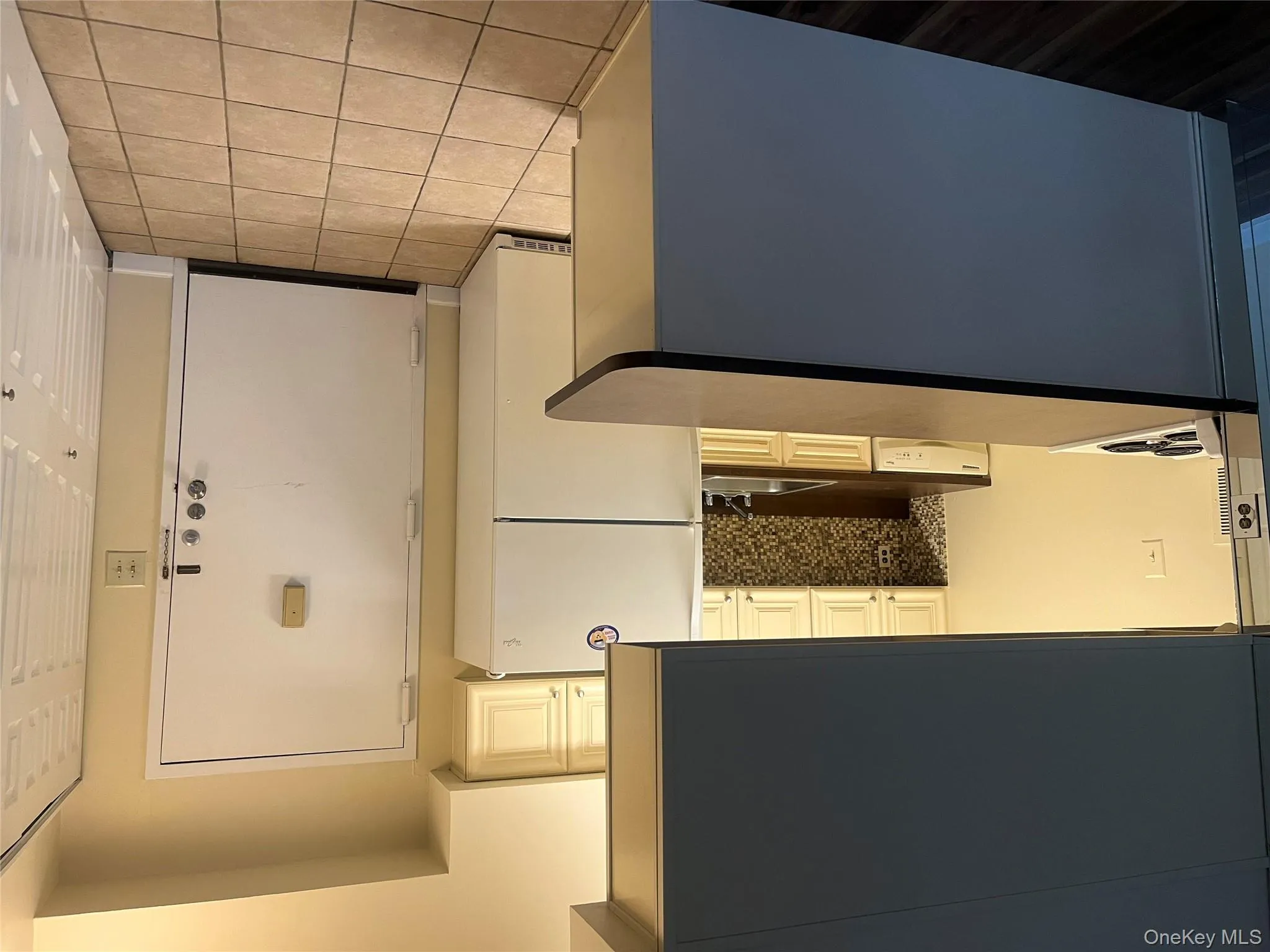 Kitchen with dark countertops, freestanding refrigerator, a peninsula, tasteful backsplash, and light tile patterned floors Kitchen with dark countertops, freestanding refrigerator, a peninsula, tasteful backsplash, and light tile patterned floors