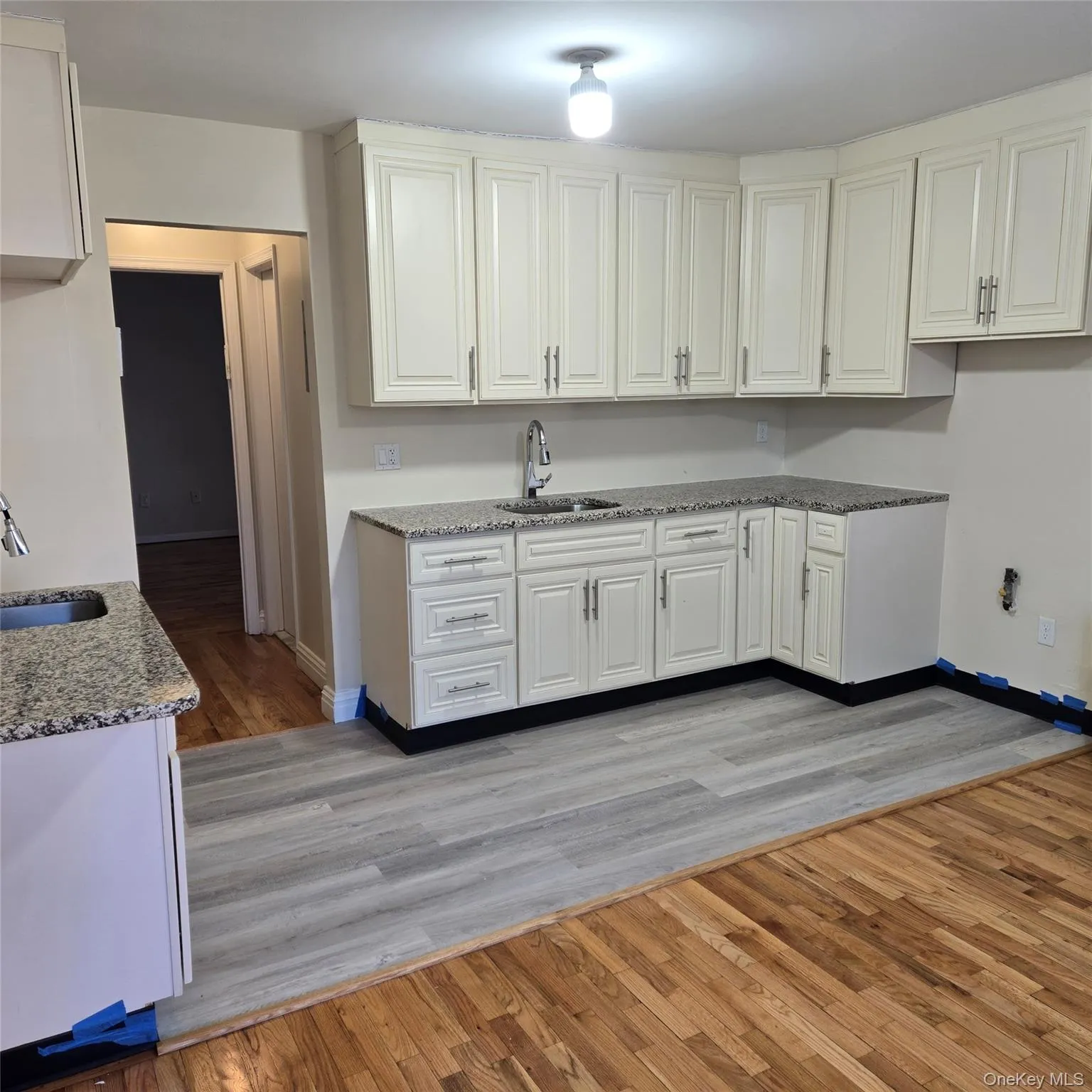 Kitchen with light wood finished floors, light stone countertops, and white cabinetry Kitchen with light wood finished floors, light stone countertops, and white cabinetry