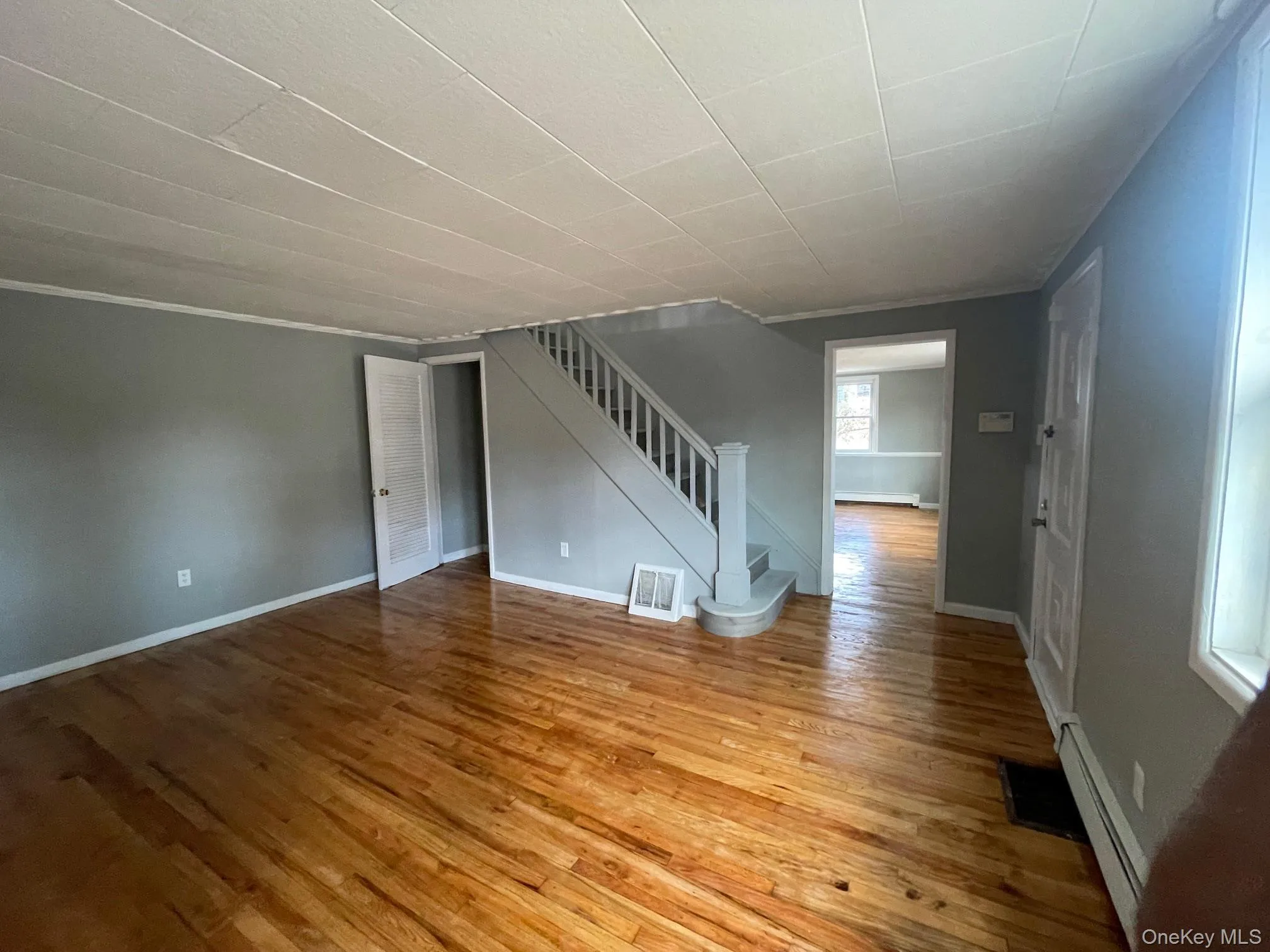 Unfurnished living room featuring stairway, light wood finished floors, baseboard heating, and crown molding Unfurnished living room featuring stairway, light wood finished floors, baseboard heating, and crown molding