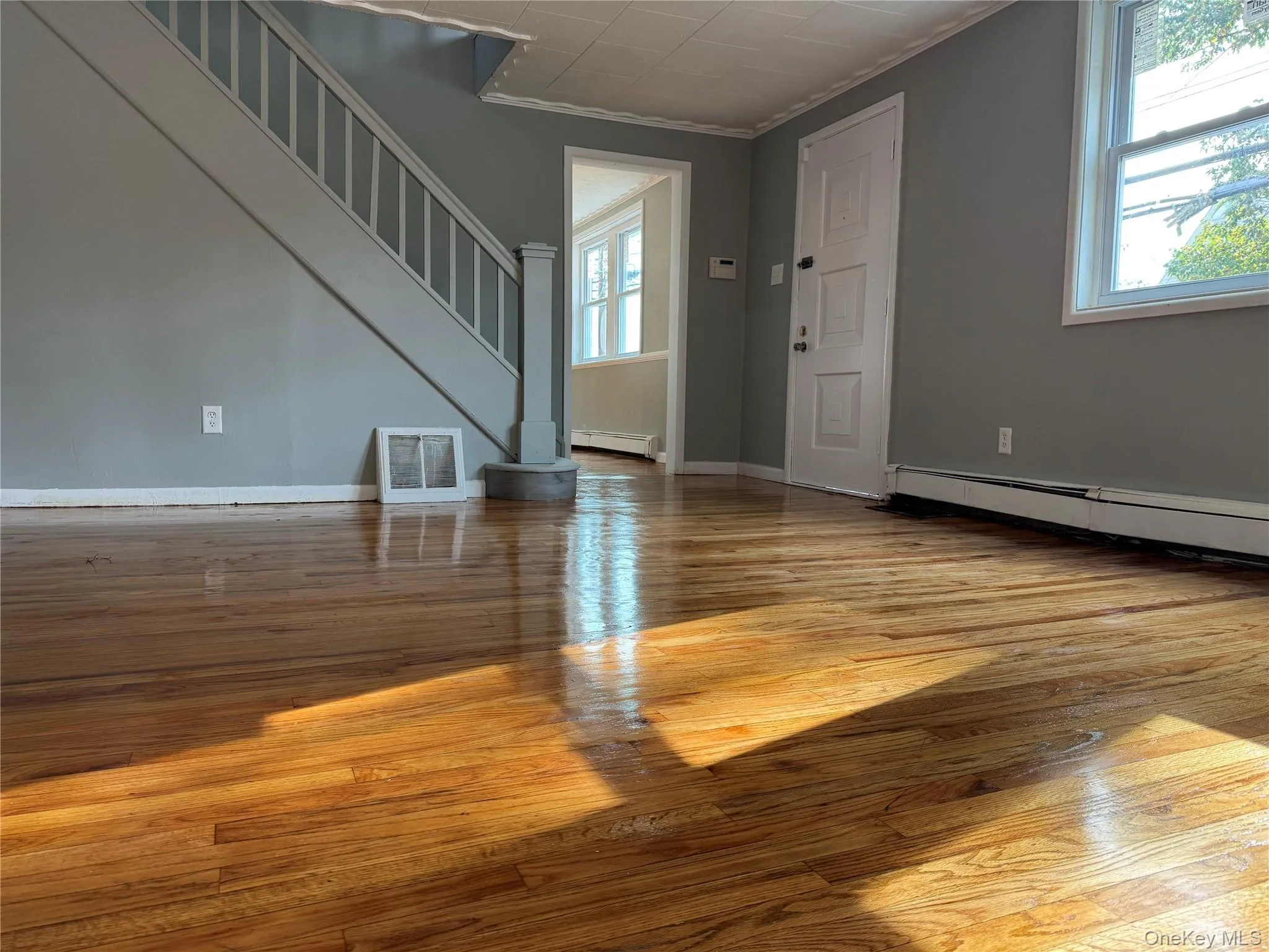 Unfurnished living room with light wood finished floors, stairway, baseboard heating, and crown molding Unfurnished living room with light wood finished floors, stairway, baseboard heating, and crown molding