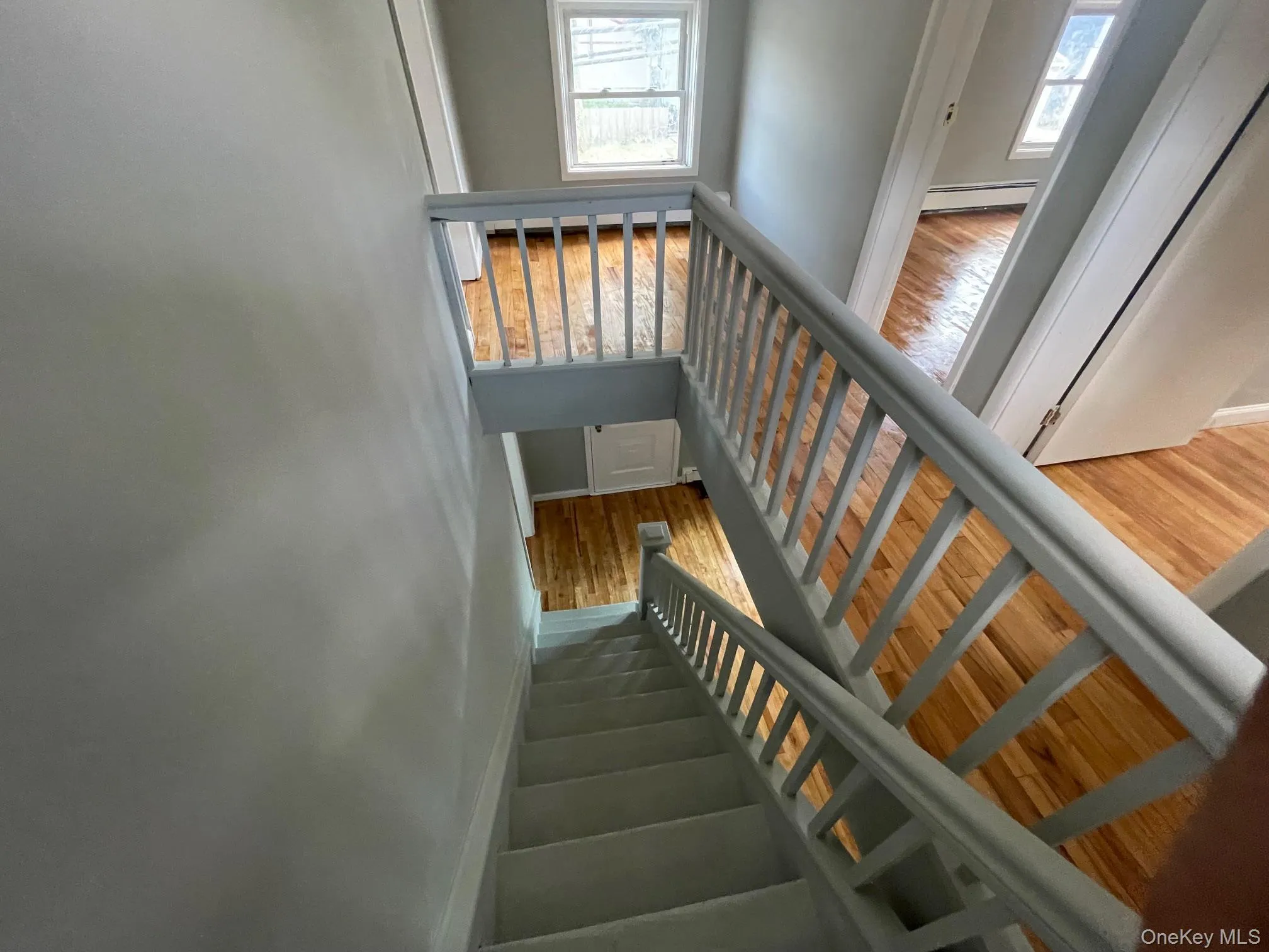 Stairs with wood finished floors, healthy amount of natural light, and baseboard heating Stairs with wood finished floors, healthy amount of natural light, and baseboard heating