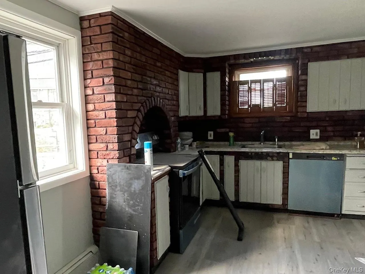 Kitchen with stainless steel appliances, a baseboard heating unit, light wood finished floors, and brick wall Kitchen with stainless steel appliances, a baseboard heating unit, light wood finished floors, and brick wall