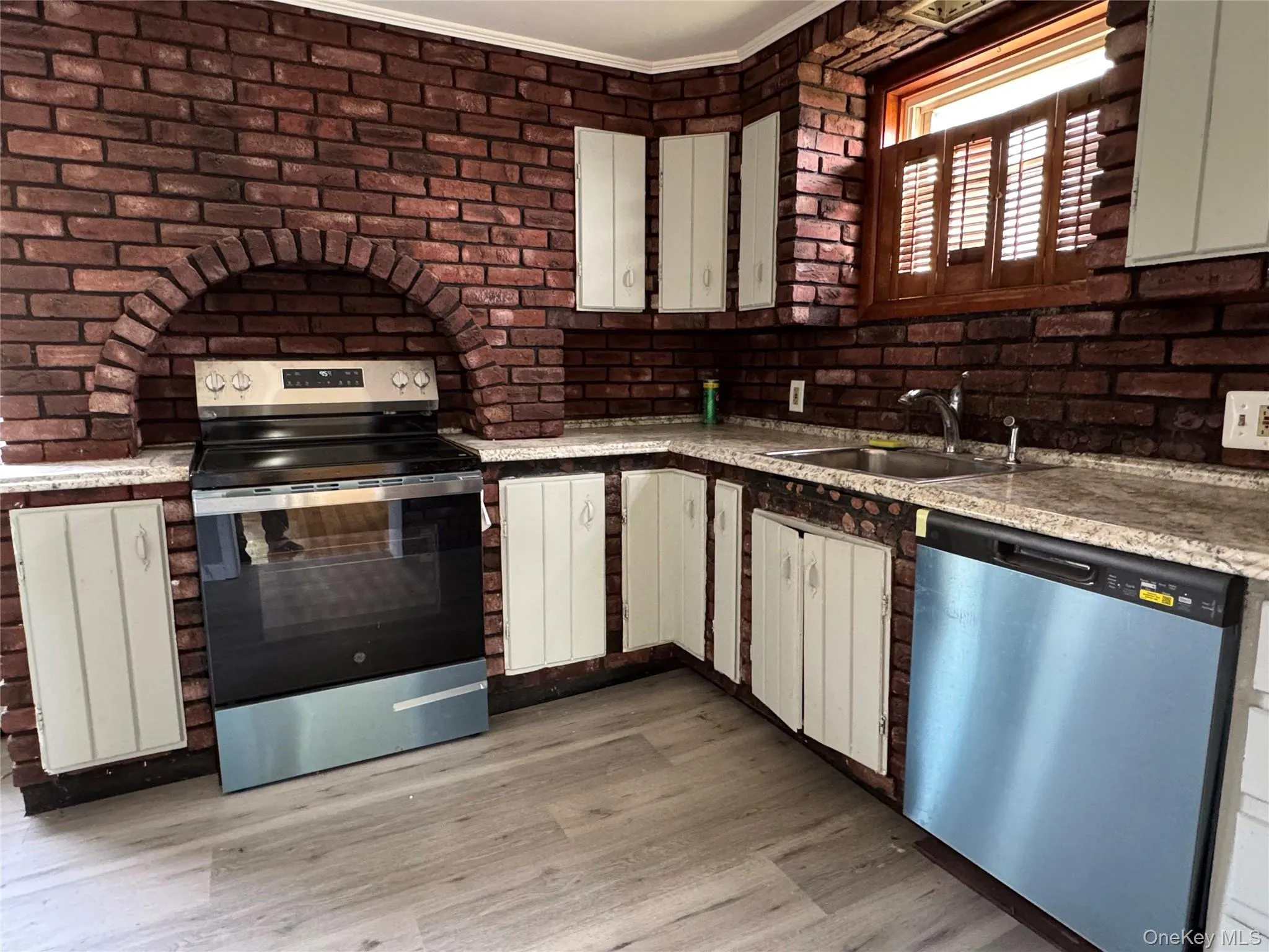 Kitchen with appliances with stainless steel finishes, light wood-style flooring, brick wall, and white cabinets Kitchen with appliances with stainless steel finishes, light wood-style flooring, brick wall, and white cabinets