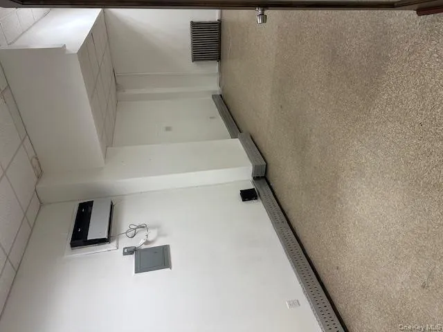 Below grade area with a paneled ceiling, radiator heating unit, electric panel, and a wall unit AC Below grade area with a paneled ceiling, radiator heating unit, electric panel, and a wall unit AC