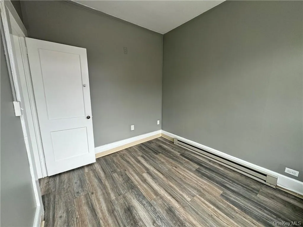 Unfurnished room with dark wood-type flooring and a baseboard radiator Unfurnished room with dark wood-type flooring and a baseboard radiator