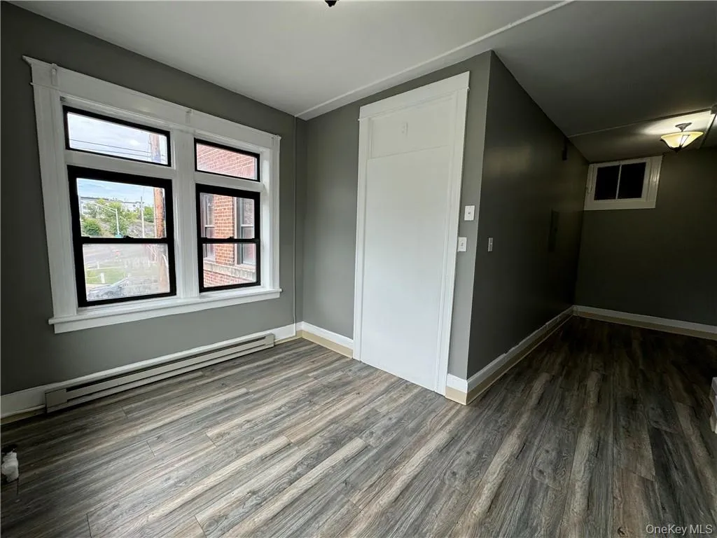 Empty room with dark hardwood / wood-style flooring and a baseboard radiator Empty room with dark hardwood / wood-style flooring and a baseboard radiator