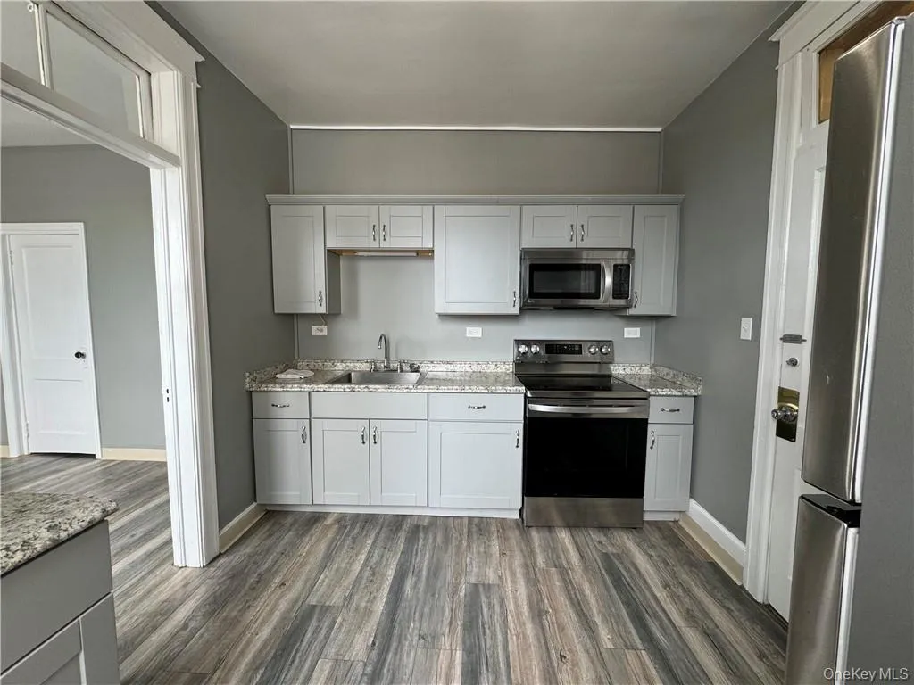 Kitchen featuring appliances with stainless steel finishes, sink, light stone countertops, and dark hardwood / wood-style floors Kitchen featuring appliances with stainless steel finishes, sink, light stone countertops, and dark hardwood / wood-style floors