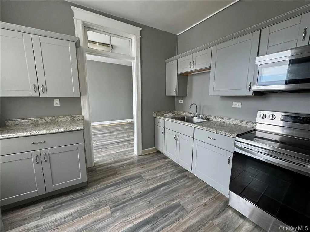 Kitchen with wood-type flooring, light stone counters, stainless steel appliances, and sink Kitchen with wood-type flooring, light stone counters, stainless steel appliances, and sink