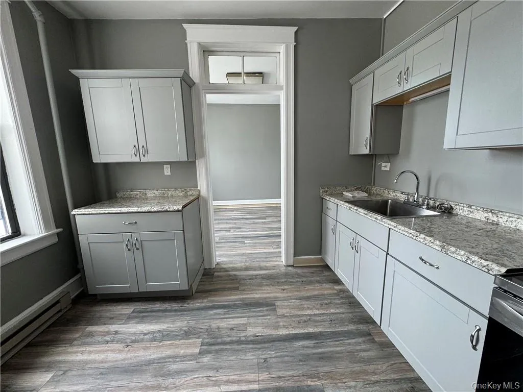 Kitchen with gray cabinetry, a baseboard heating unit, stainless steel range oven, sink, and wood-type flooring Kitchen with gray cabinetry, a baseboard heating unit, stainless steel range oven, sink, and wood-type flooring