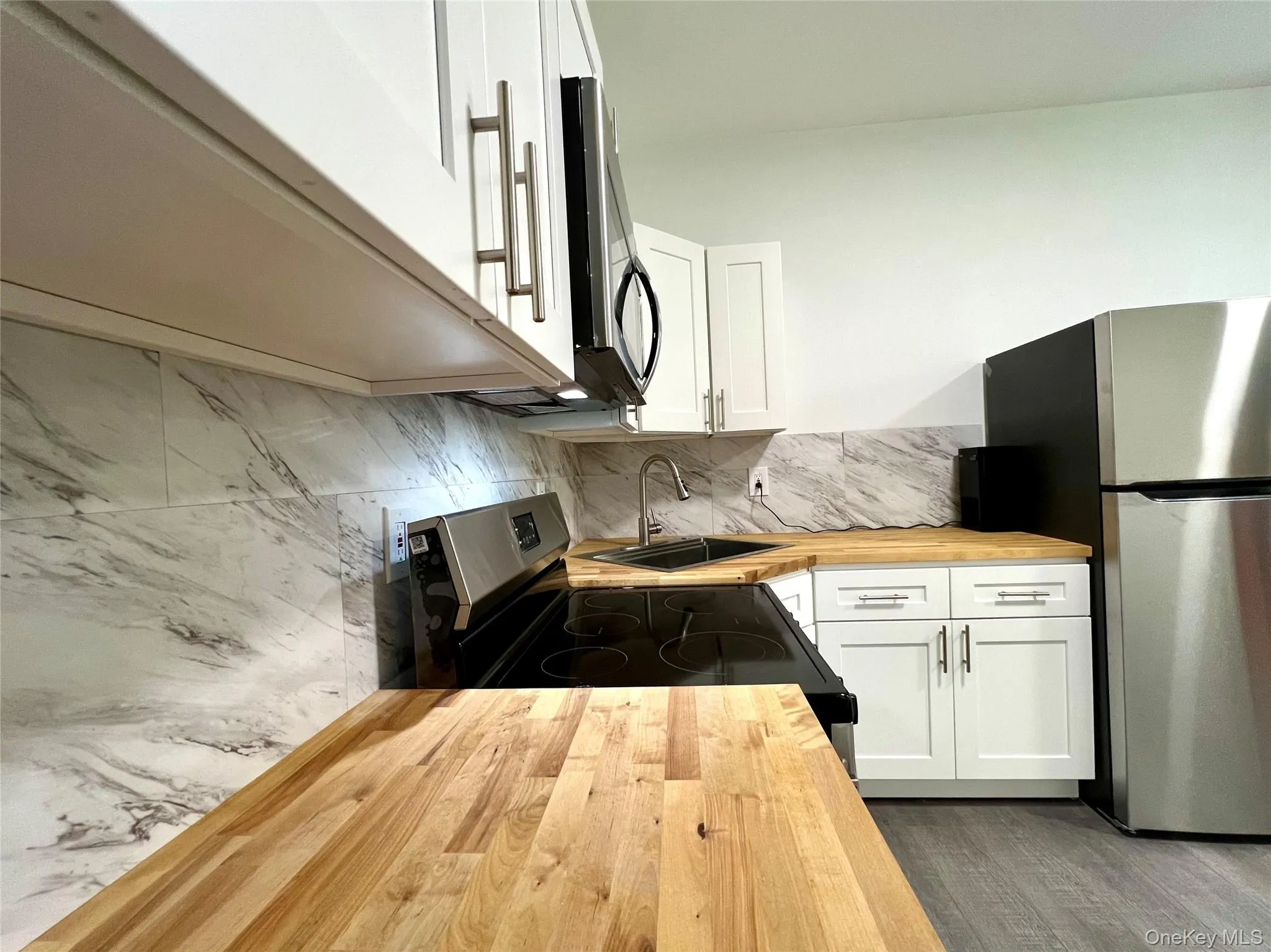 Kitchen with butcher block counters, white cabinets, appliances with stainless steel finishes, tasteful backsplash, and dark wood-style floors Kitchen with butcher block counters, white cabinets, appliances with stainless steel finishes, tasteful backsplash, and dark wood-style floors