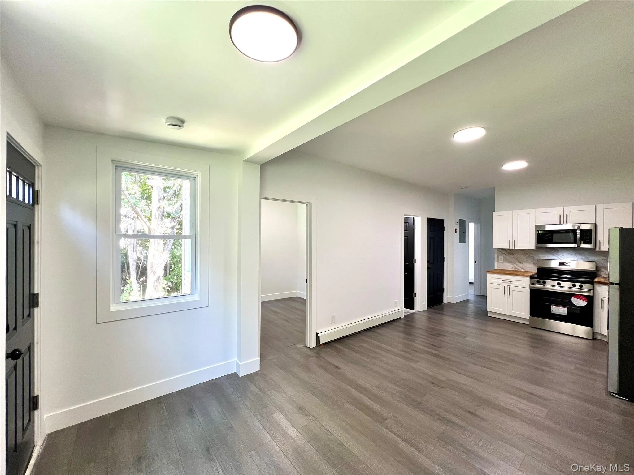 Kitchen featuring white cabinets, appliances with stainless steel finishes, tasteful backsplash, dark wood-style floors, and butcher block countertops Kitchen featuring white cabinets, appliances with stainless steel finishes, tasteful backsplash, dark wood-style floors, and butcher block countertops