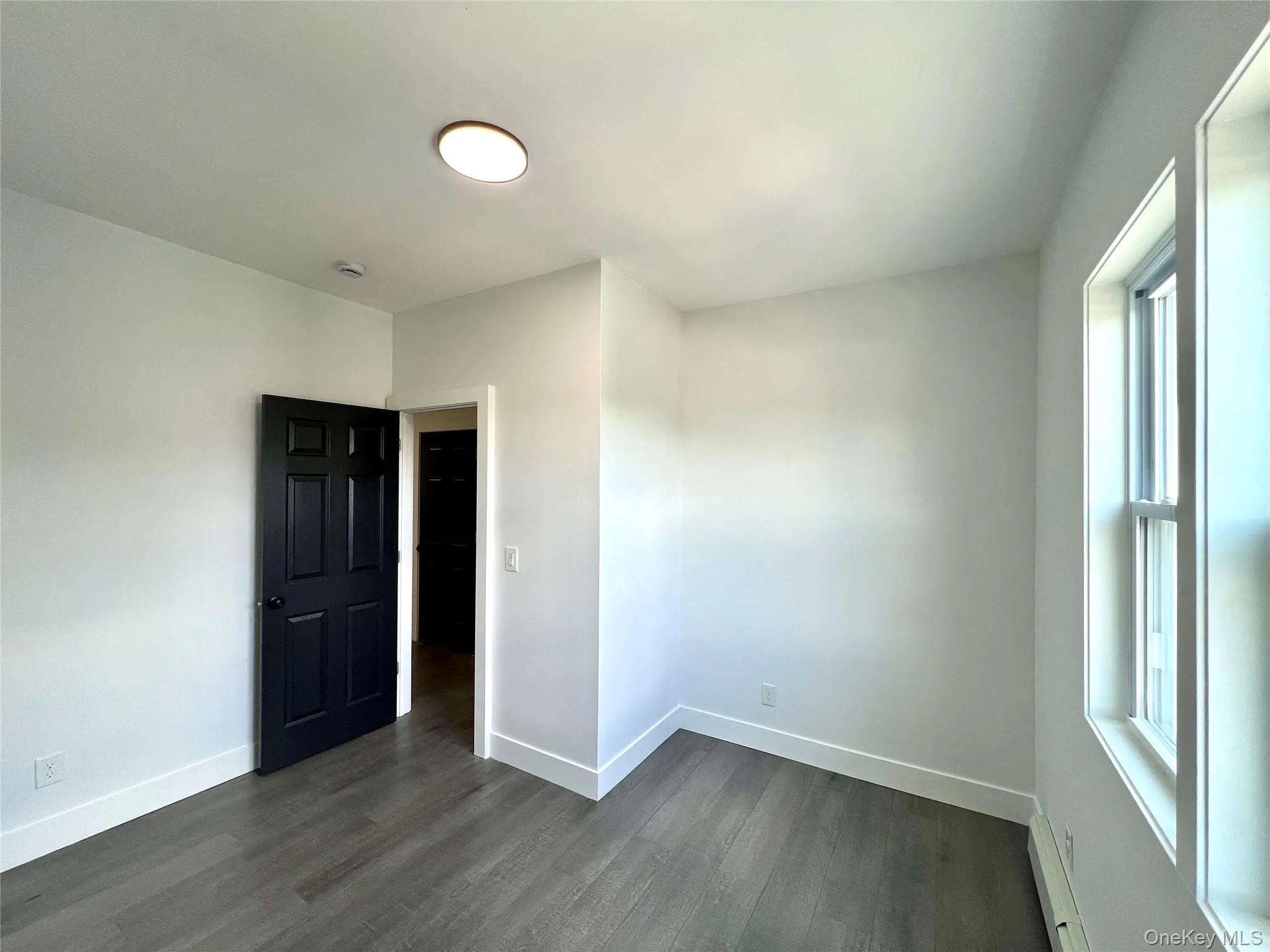 Unfurnished bedroom with dark wood-type flooring and baseboard heating Unfurnished bedroom with dark wood-type flooring and baseboard heating