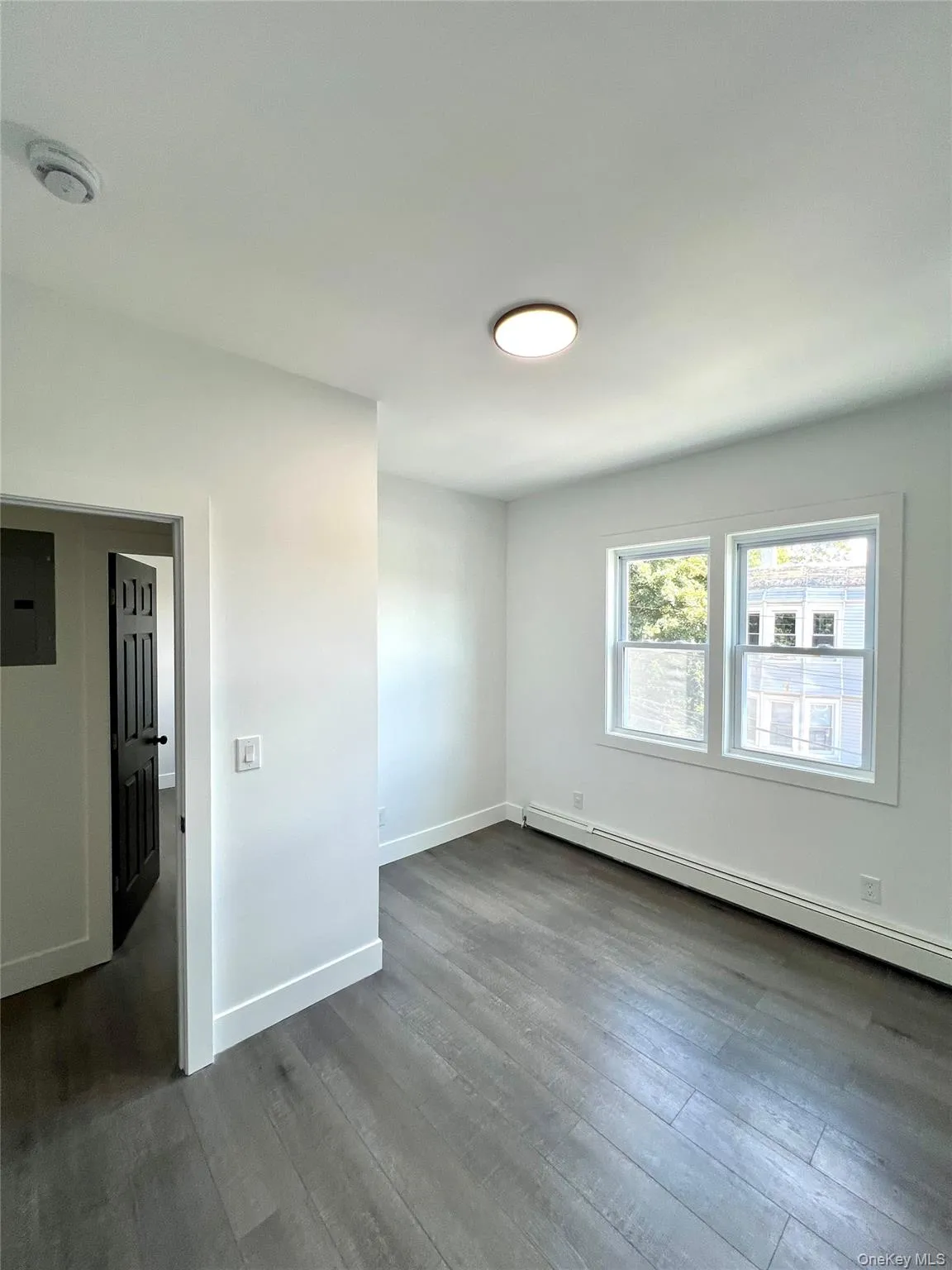 Unfurnished bedroom with a baseboard heating unit, dark wood-style flooring, and electric panel Unfurnished bedroom with a baseboard heating unit, dark wood-style flooring, and electric panel