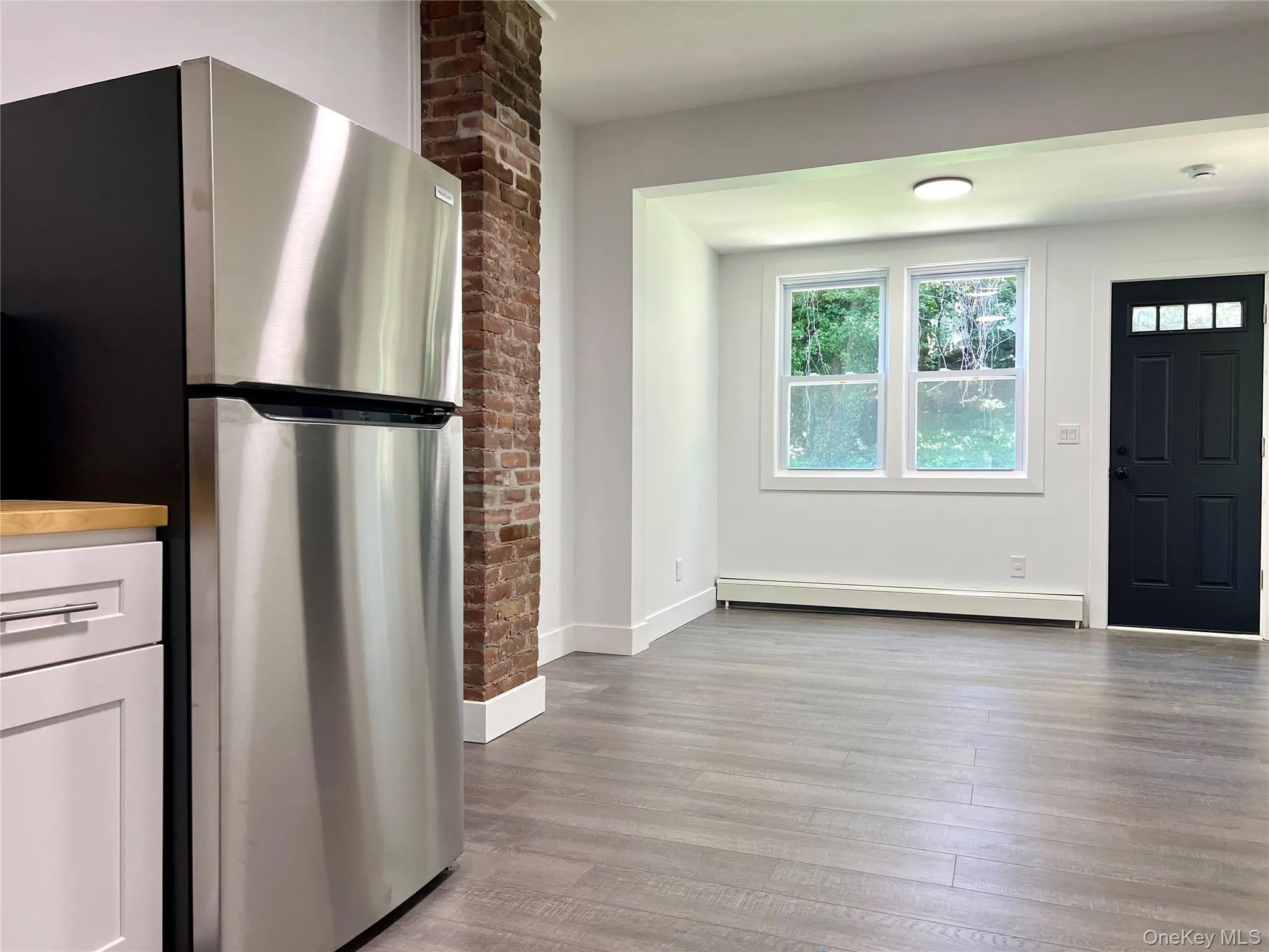 Kitchen with freestanding refrigerator, light wood-style floors, a baseboard radiator, and white cabinetry Kitchen with freestanding refrigerator, light wood-style floors, a baseboard radiator, and white cabinetry