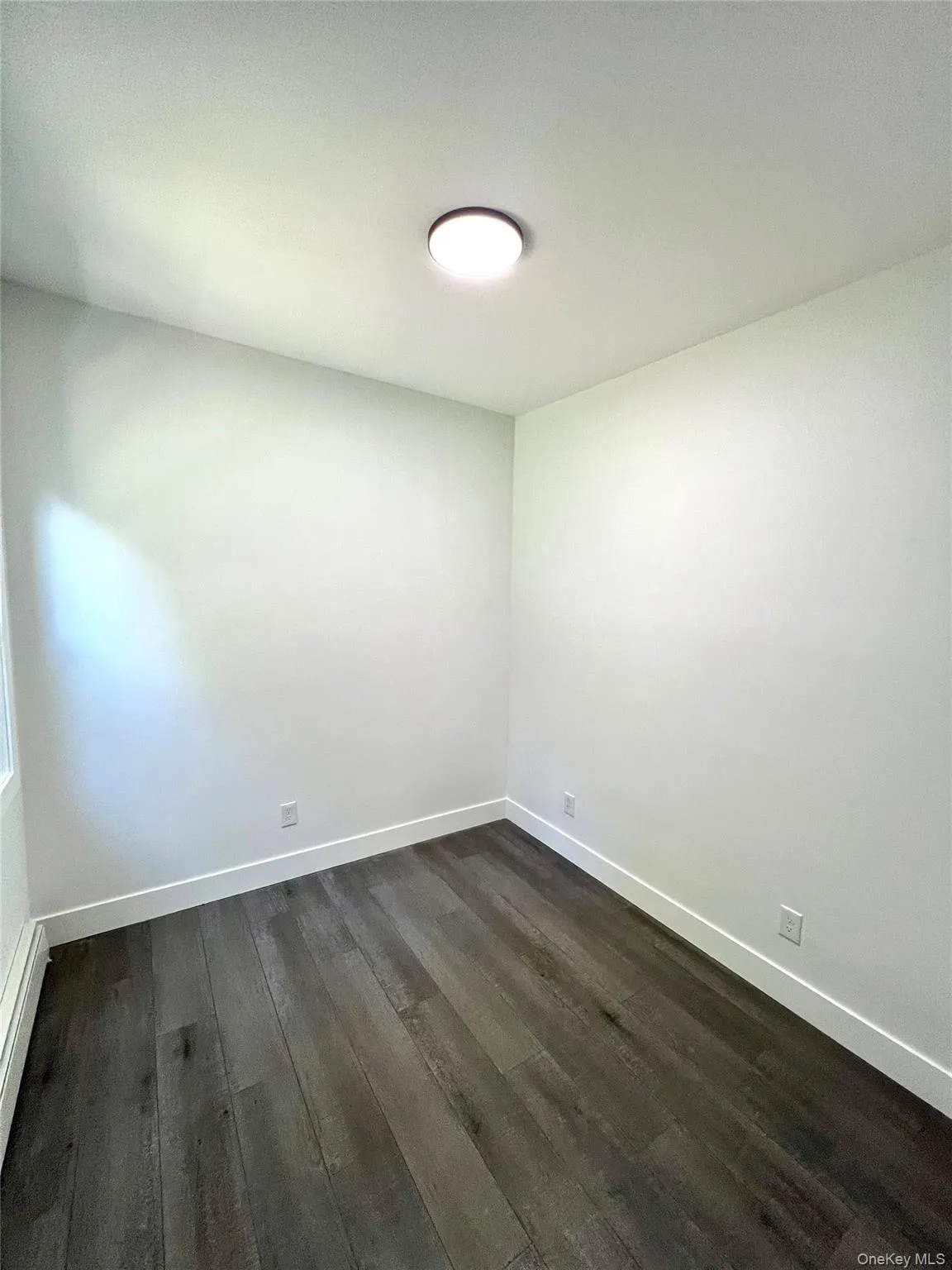 Spare room with dark wood-style flooring and baseboard heating Spare room with dark wood-style flooring and baseboard heating