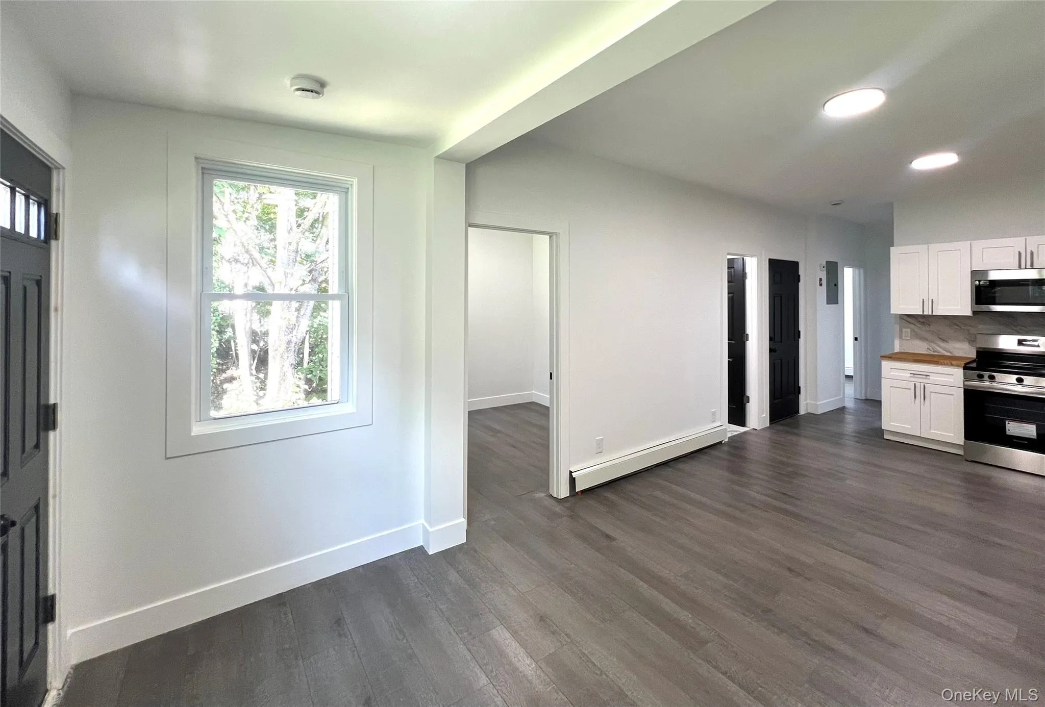 Kitchen featuring white cabinets, stainless steel appliances, dark wood-style floors, a baseboard heating unit, and decorative backsplash Kitchen featuring white cabinets, stainless steel appliances, dark wood-style floors, a baseboard heating unit, and decorative backsplash
