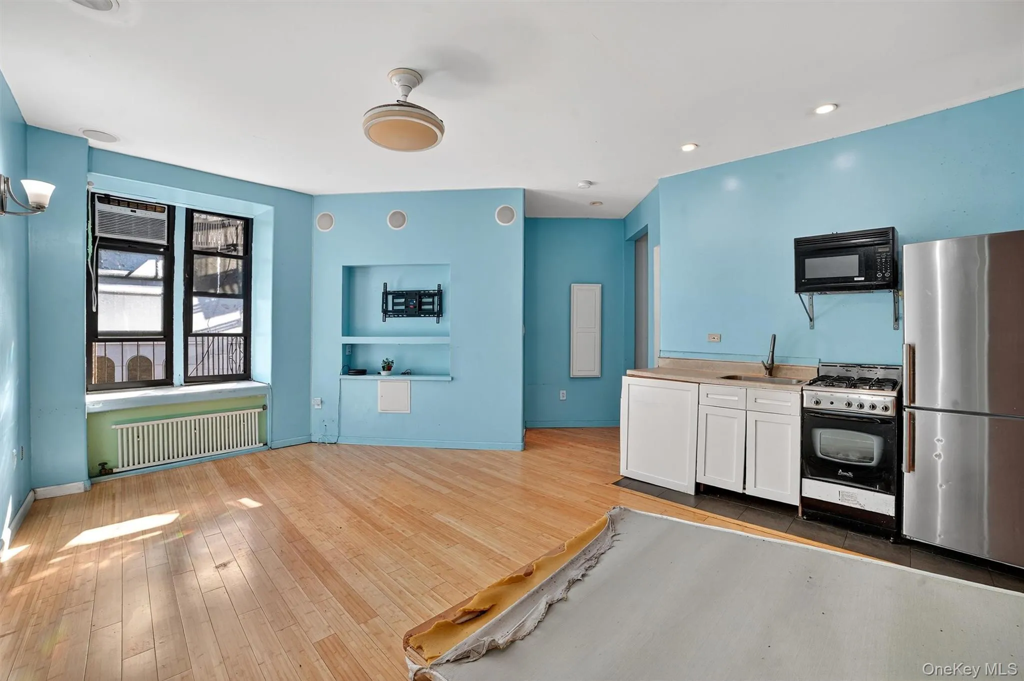 Kitchen featuring freestanding refrigerator, gas range oven, white cabinetry, radiator heating unit, and black microwave Kitchen featuring freestanding refrigerator, gas range oven, white cabinetry, radiator heating unit, and black microwave