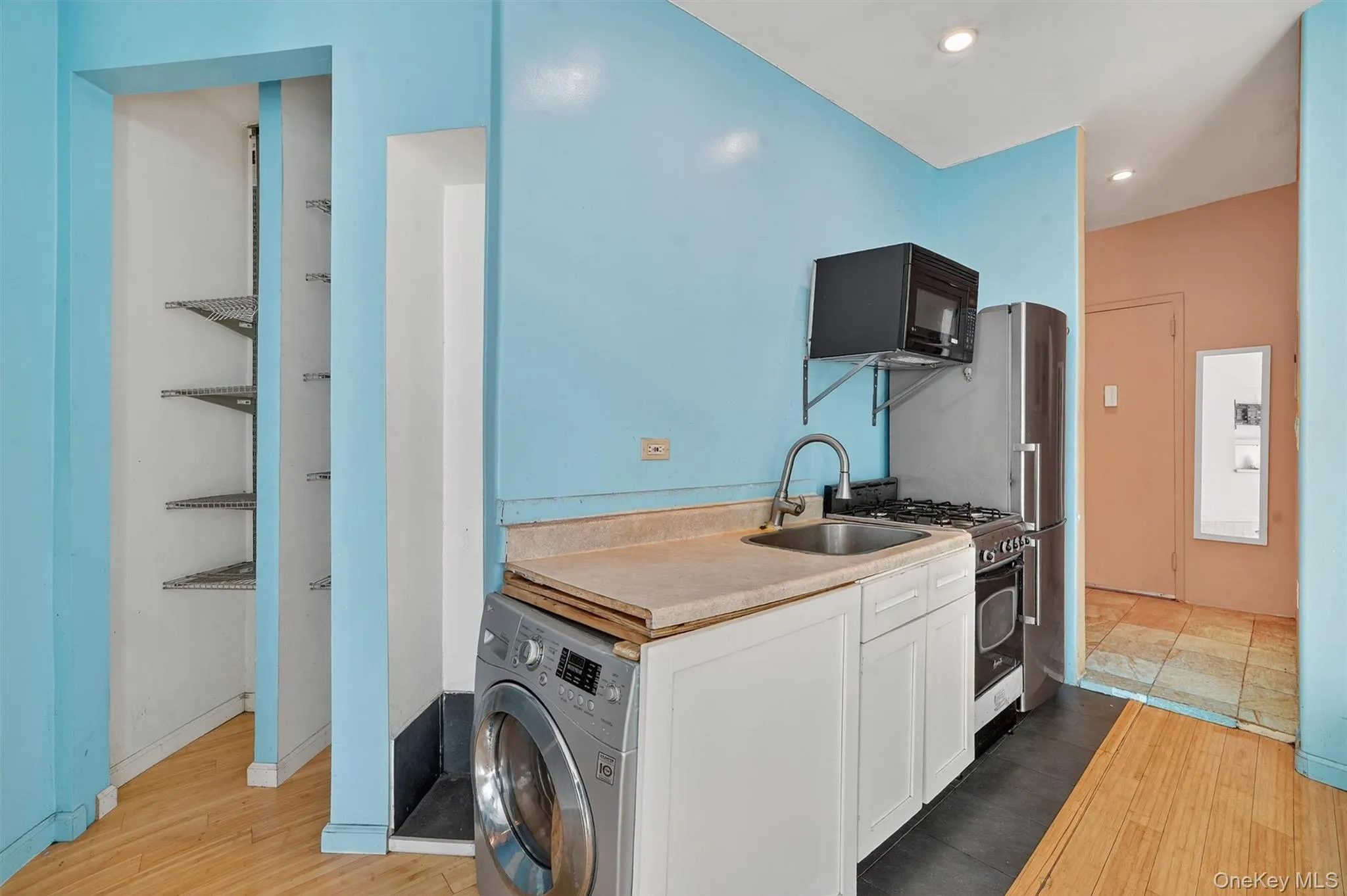 Kitchen with washer / dryer, light wood-style floors, stainless steel appliances, white cabinetry, and recessed lighting Kitchen with washer / dryer, light wood-style floors, stainless steel appliances, white cabinetry, and recessed lighting