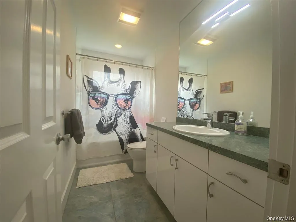 Bathroom featuring vanity, shower / tub combo, and dark tile patterned flooring Bathroom featuring vanity, shower / tub combo, and dark tile patterned flooring