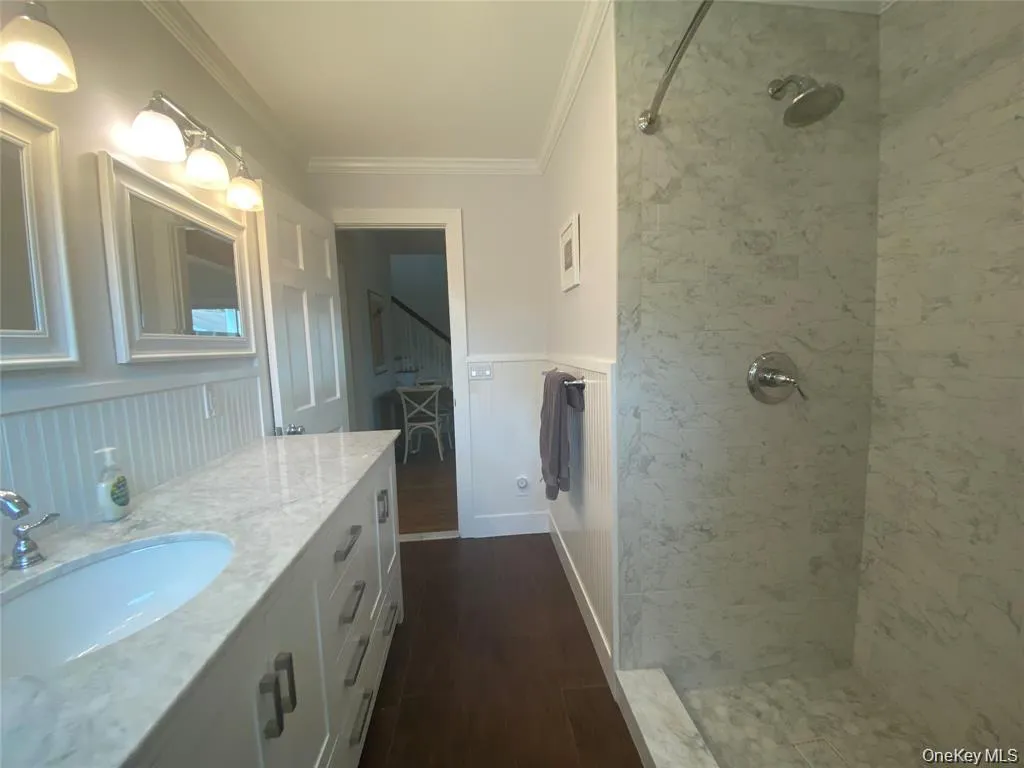 Bathroom with dark wood-style flooring, crown molding, a tile shower, and vanity Bathroom with dark wood-style flooring, crown molding, a tile shower, and vanity