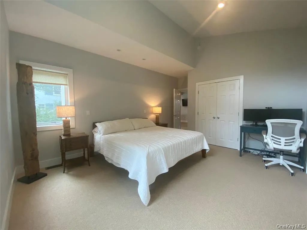 Bedroom with a closet, carpet flooring, vaulted ceiling, and an office area Bedroom with a closet, carpet flooring, vaulted ceiling, and an office area